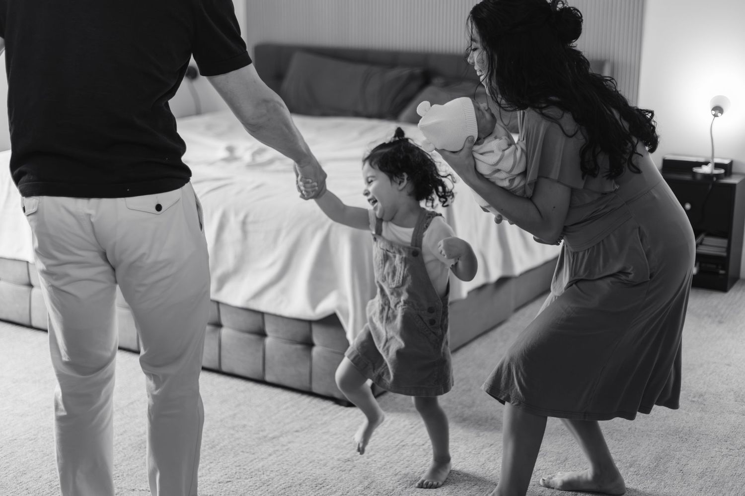 Black and white photo of parents playing with toddler daughter, holding hands and dancing together taken by Minneapolis photographer