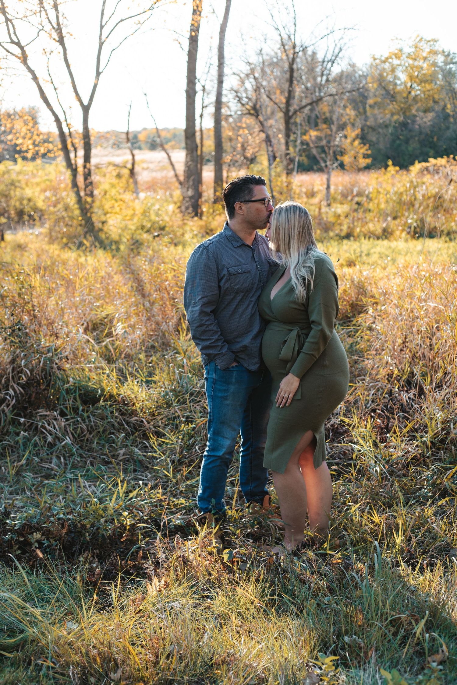 Pregnant couple shares an intimate moment in a golden field surrounded by tall grass and trees at sunset during Lakeville fall mini session.