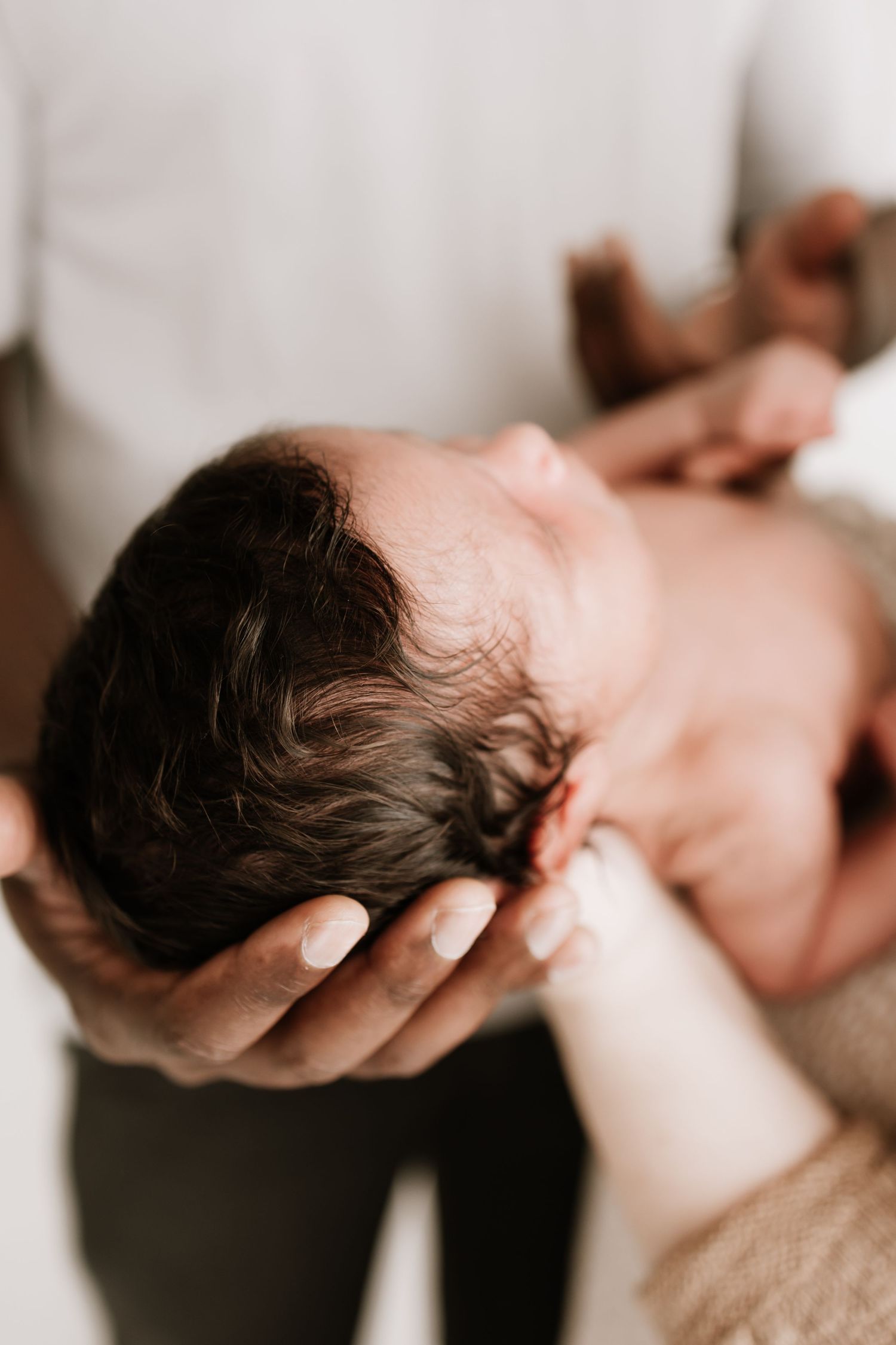 Newborn baby with dark hair cradled gently in parents hands, close-up lifestyle photography captured by Woodbury photographer.