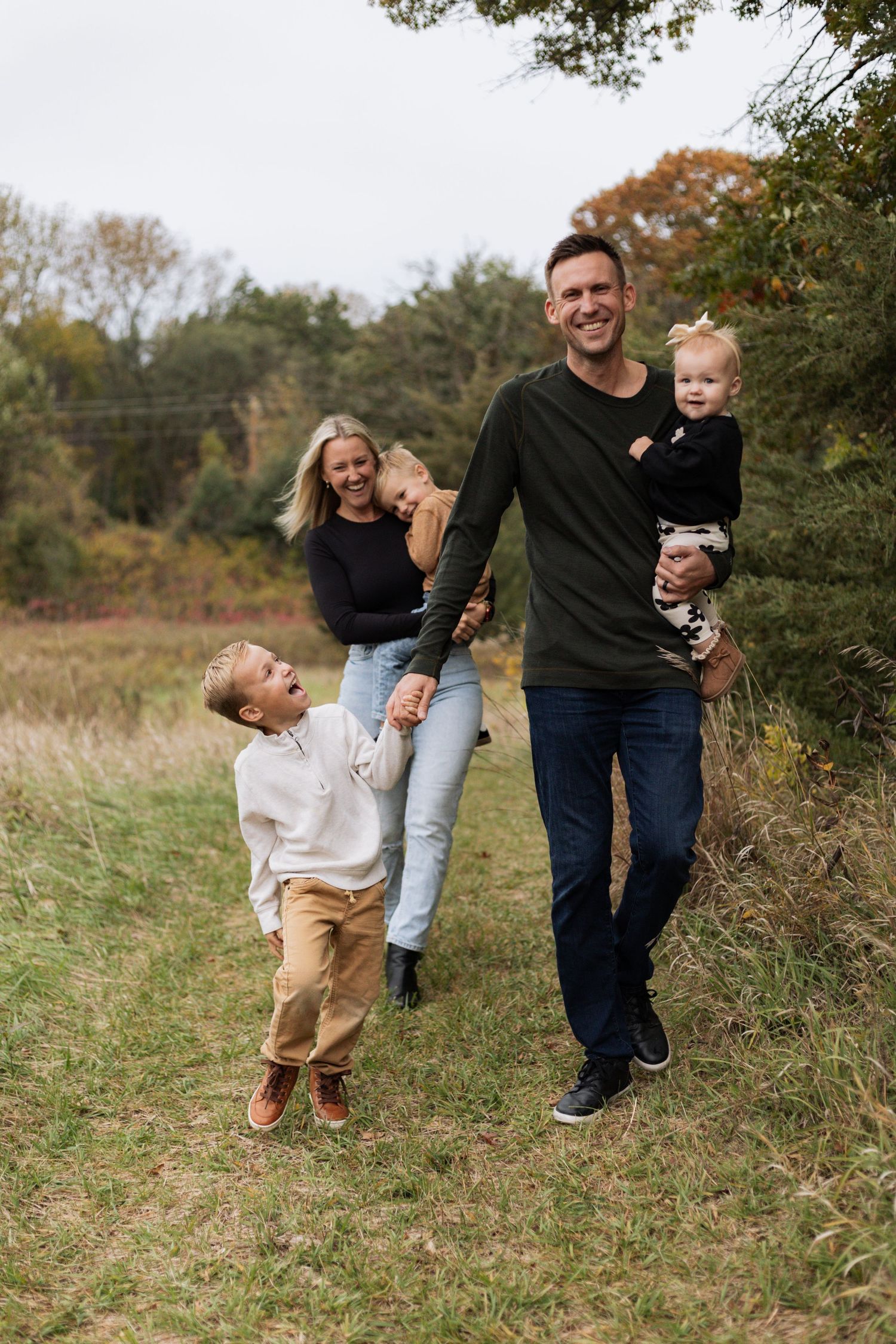 A family walks together on a grassy path during autumn with fall foliage visible in the background during Hudson fall mini session.