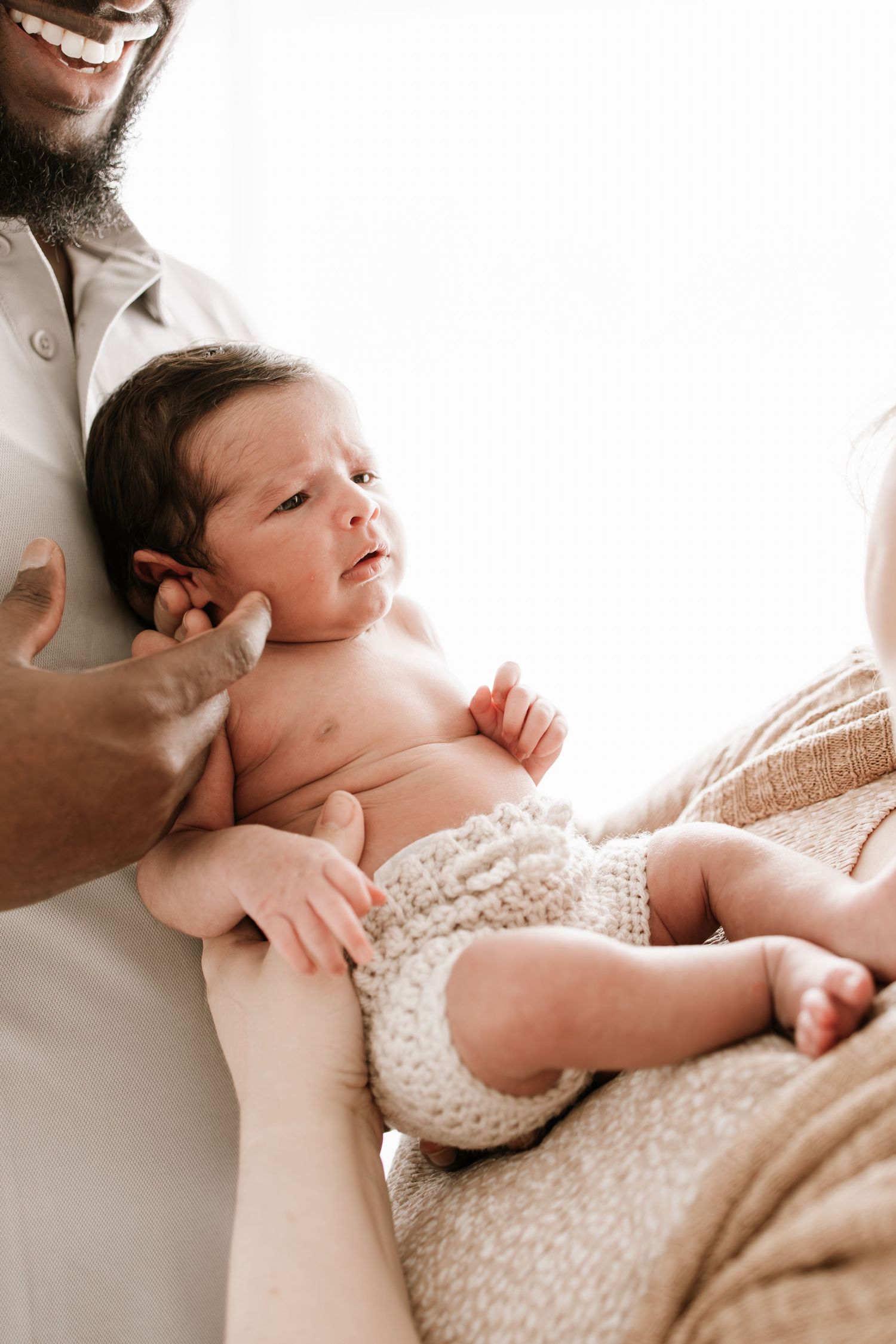 Smiling bearded father holding newborn baby wearing knit diaper cover in soft natural light.
