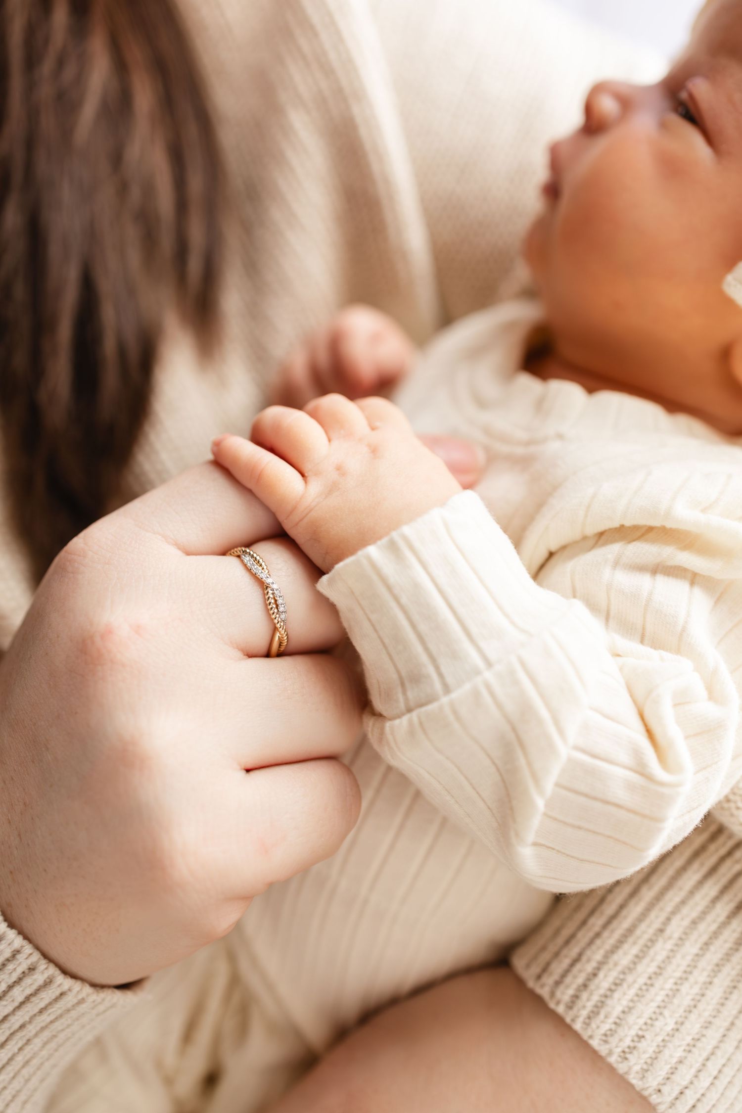 Close-up shot of a newborn wearing a cozy cream-colored knit sweater while snuggled in mother's arms during studio newborn session.