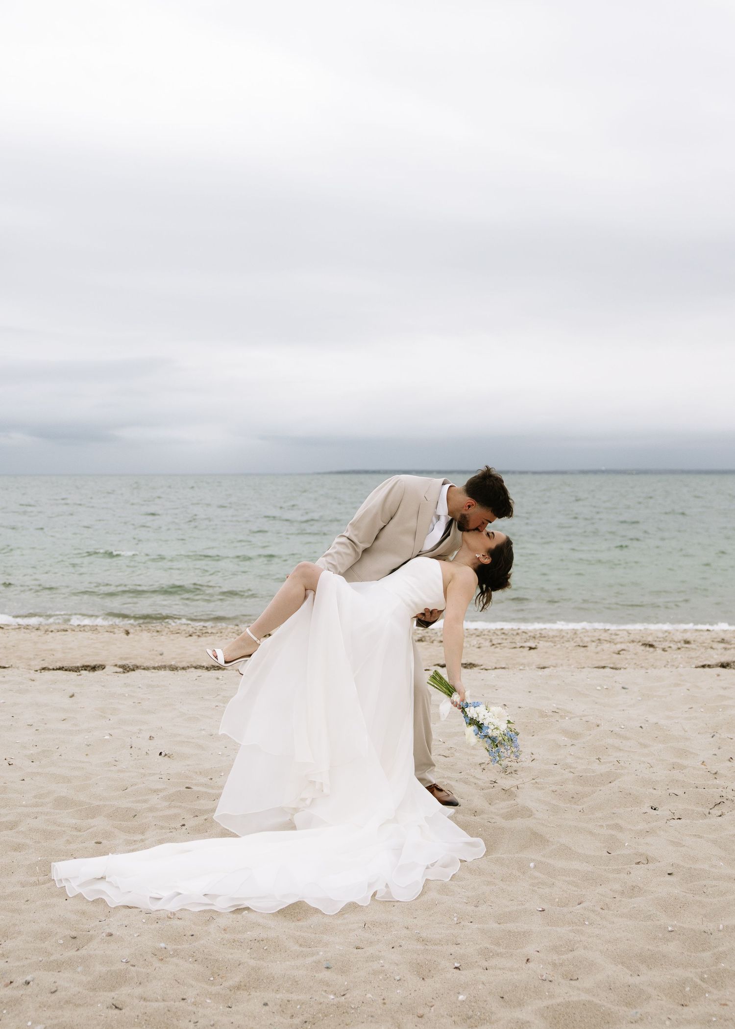 First kiss on Cape Cod beach during windy coastal elopement