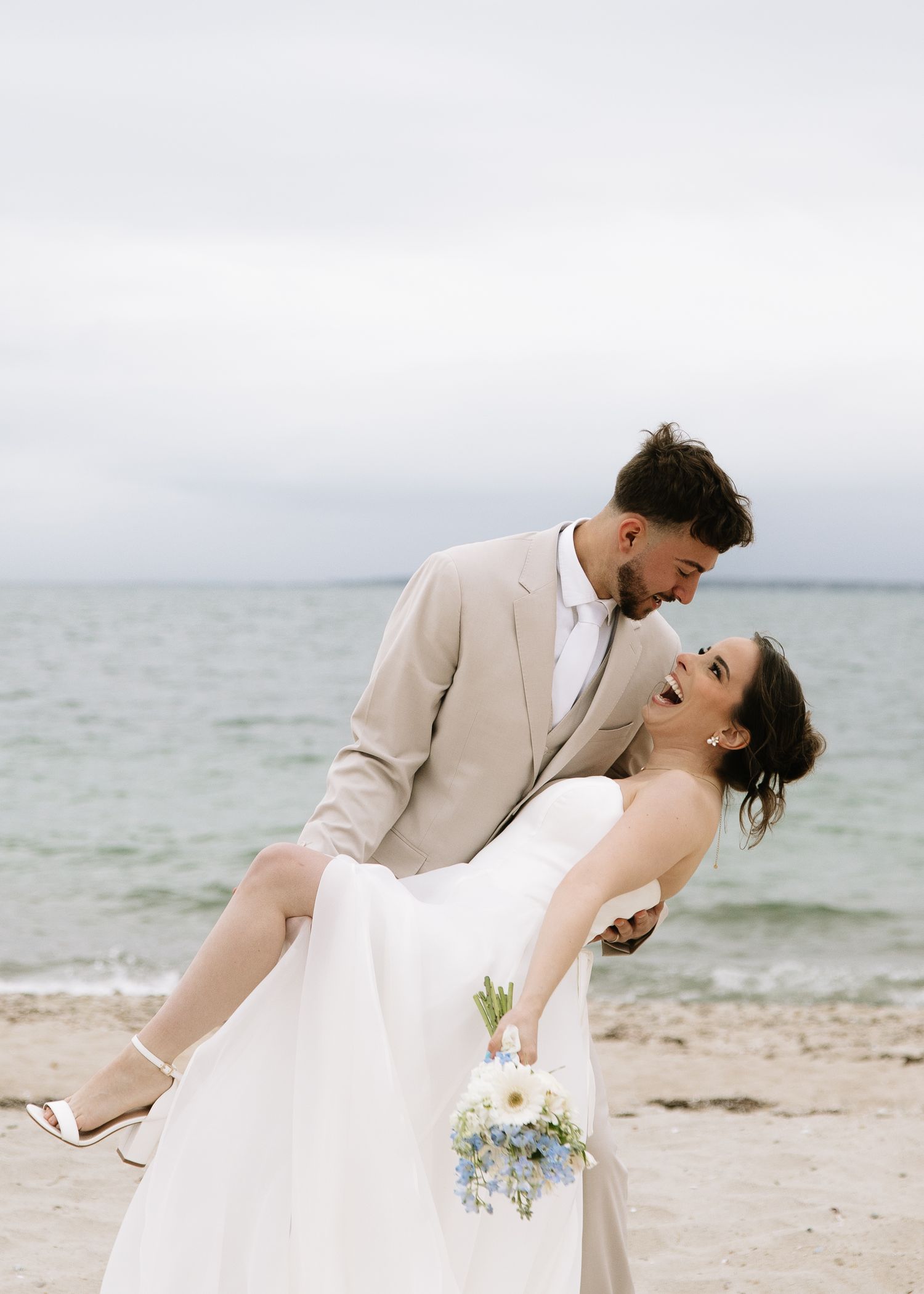 Bride and groom laughing on Cape Cod beach during windy coastal elopement