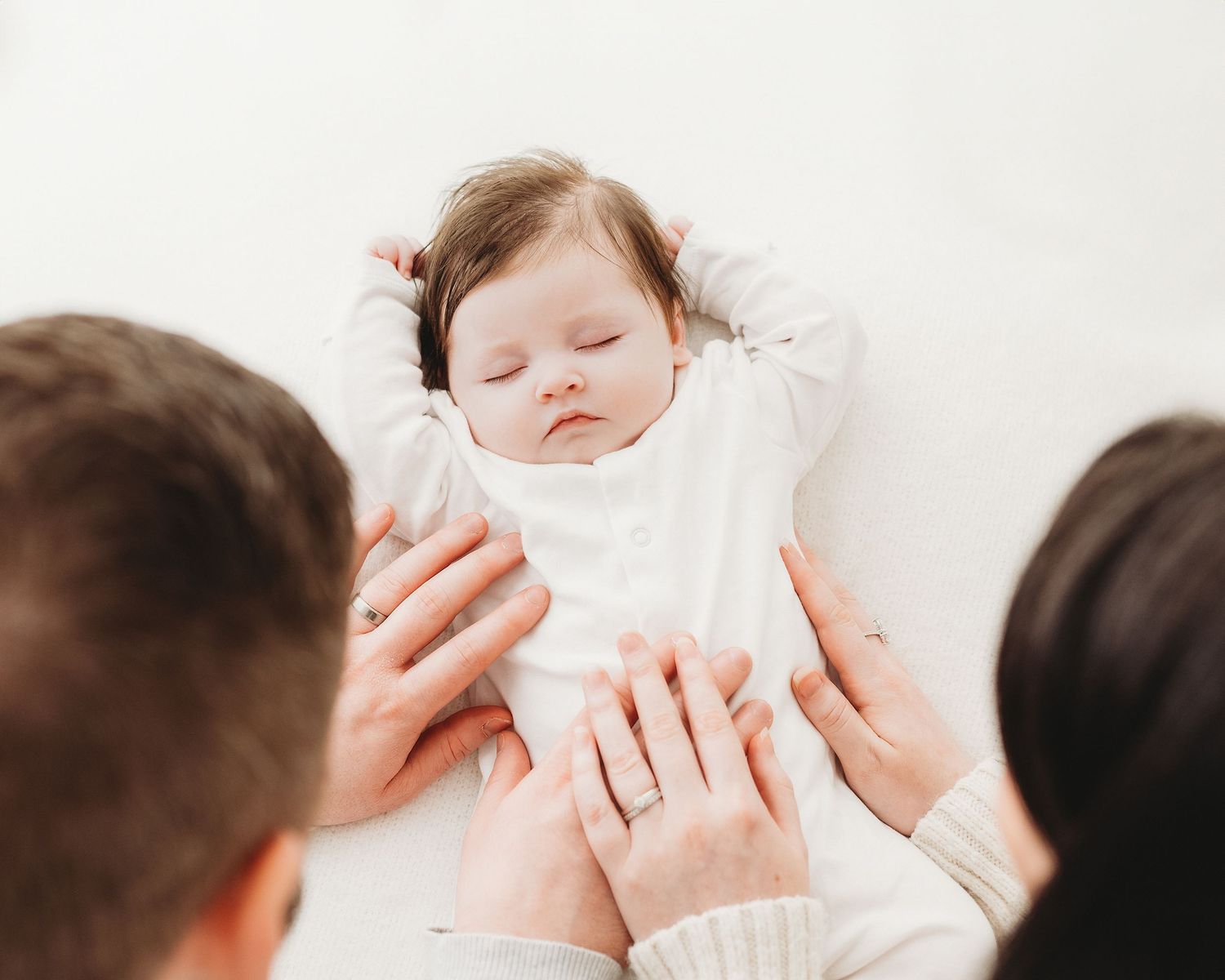 parents looking down at their sleeping 3 month old baby against a soft white background in Ayrshire photography studio