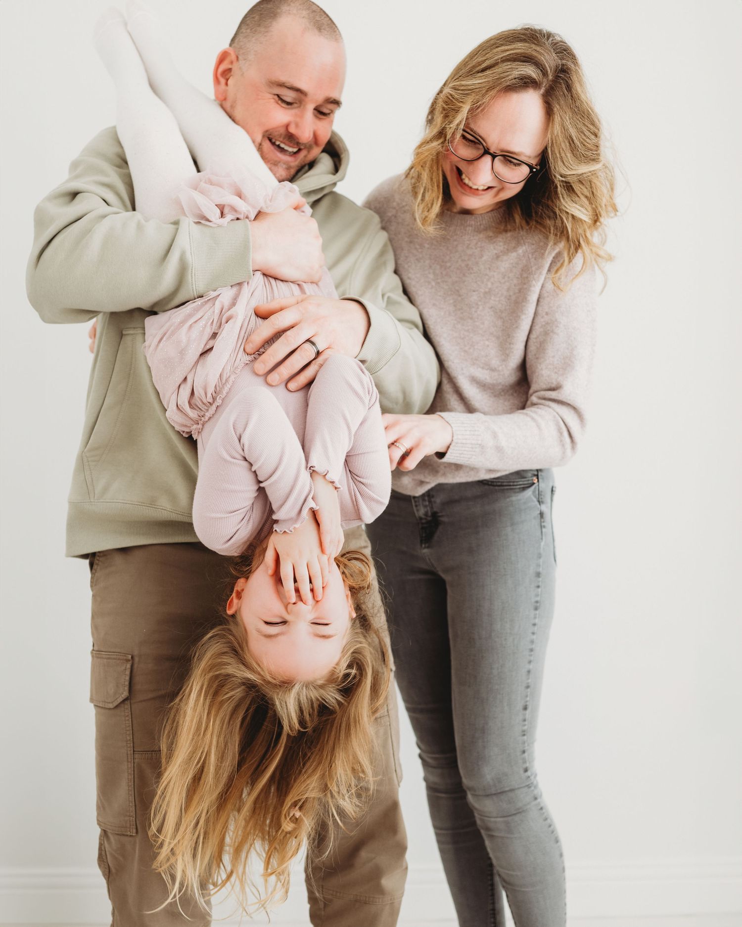 mum and dad playfully hold their daughter upside down who laughs at how much fun she is having