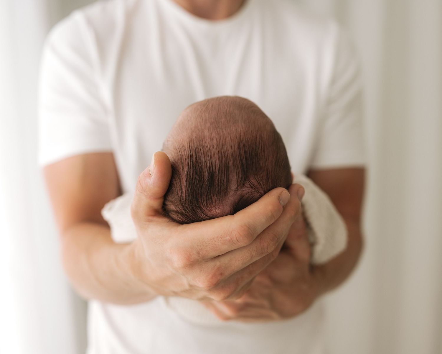 first time dad proudly cradles his tiny newborn daughter during her newborn photoshoot in Ayrshire's all-white timeless studio