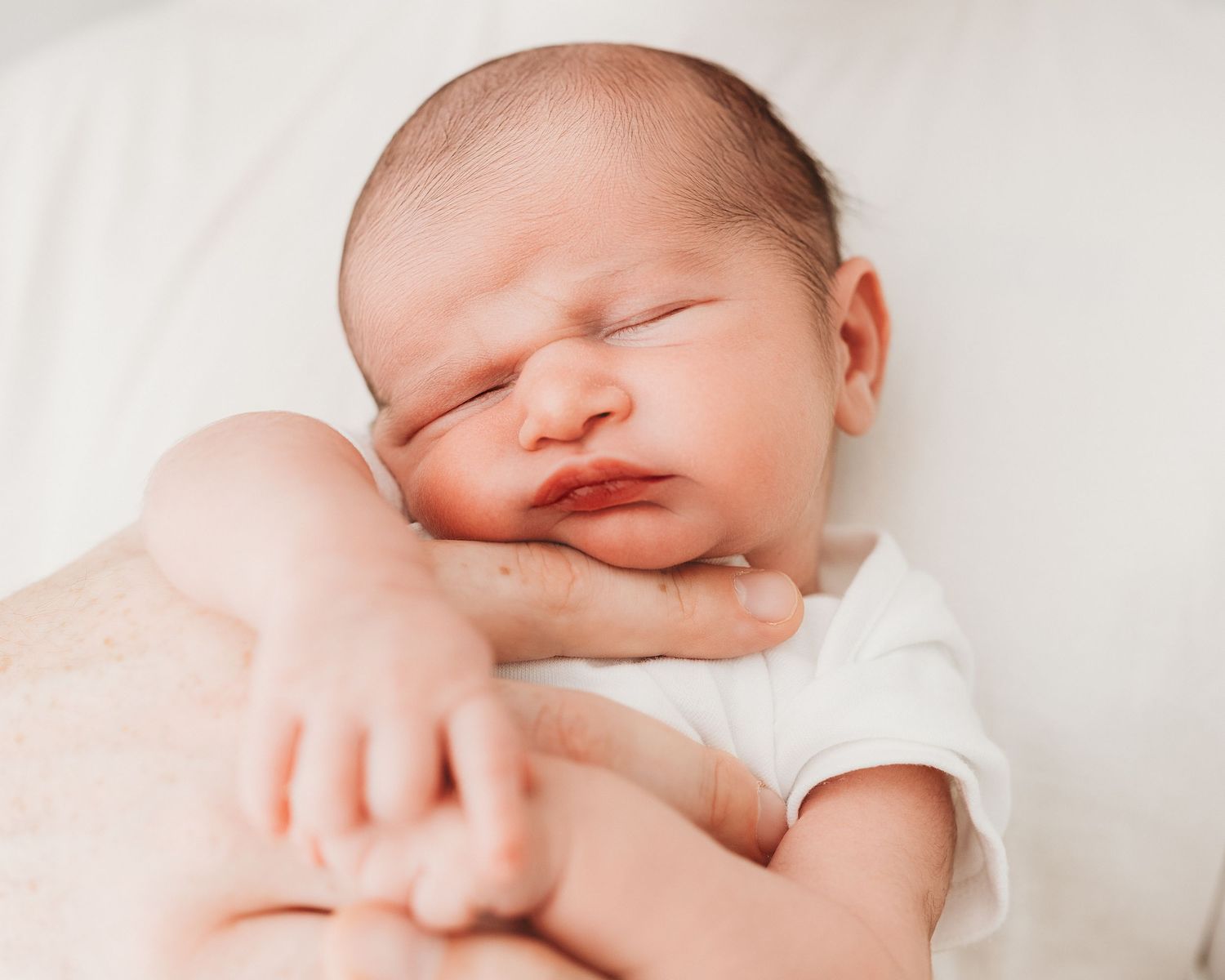 Peaceful newborn baby rests his head against his dad's hand during a natural newborn photoshoot in Ayrshire