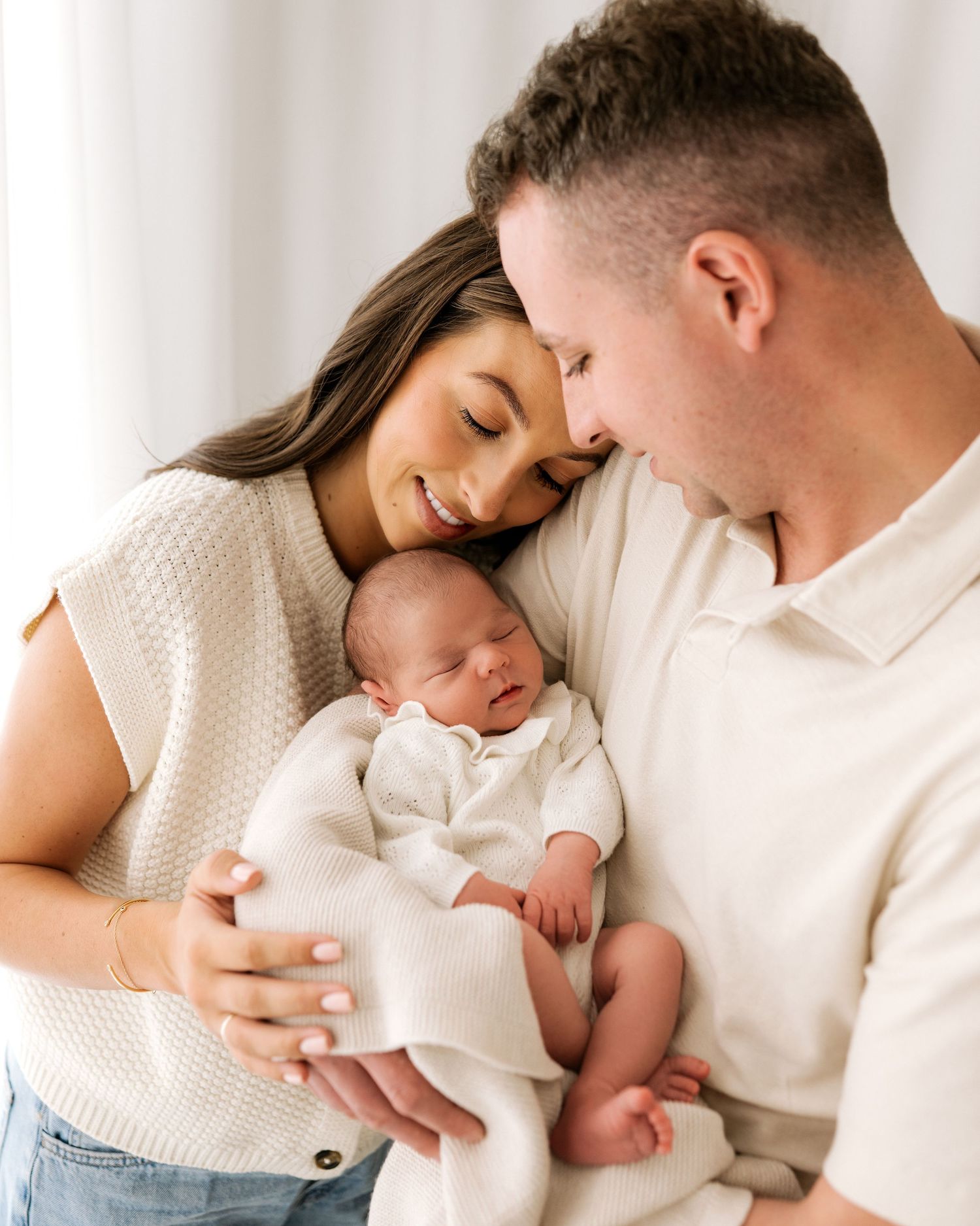 first time parents wearing soft neutral colours gaze lovingly at their sleeping newborn baby in dads arms during newborn photoshoot in Ayr