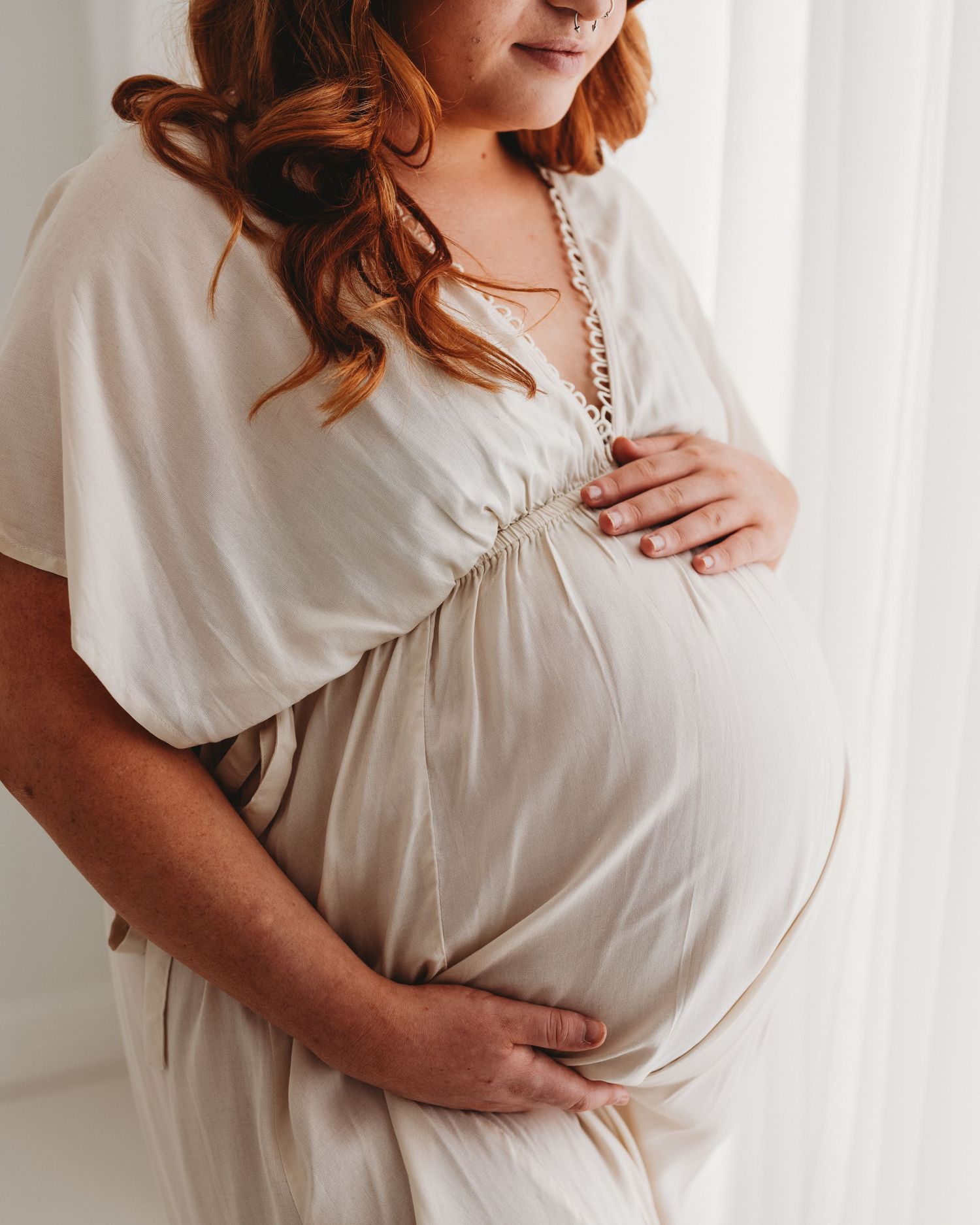 in a simple white gown, first time mum pauses during her maternity session in Ayrshire to reflect on the exciting times ahead
