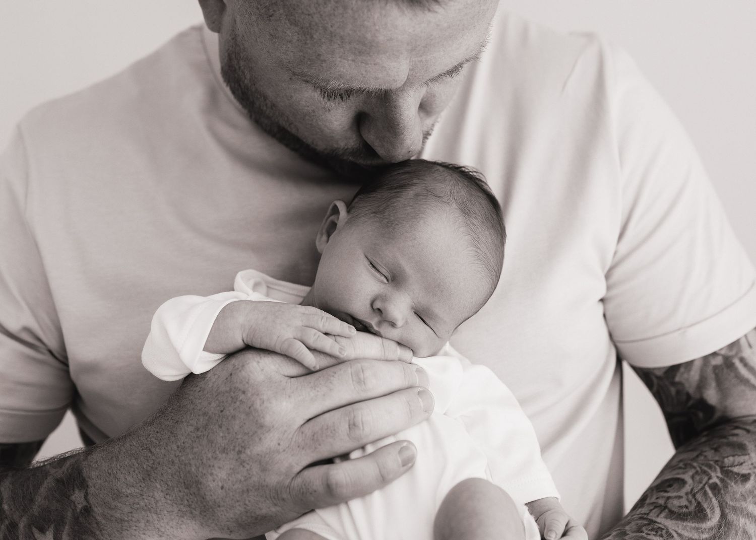 first time dad gently kisses his new daughters head as she sleeps soundly in his hands in South Ayrshire photography studio