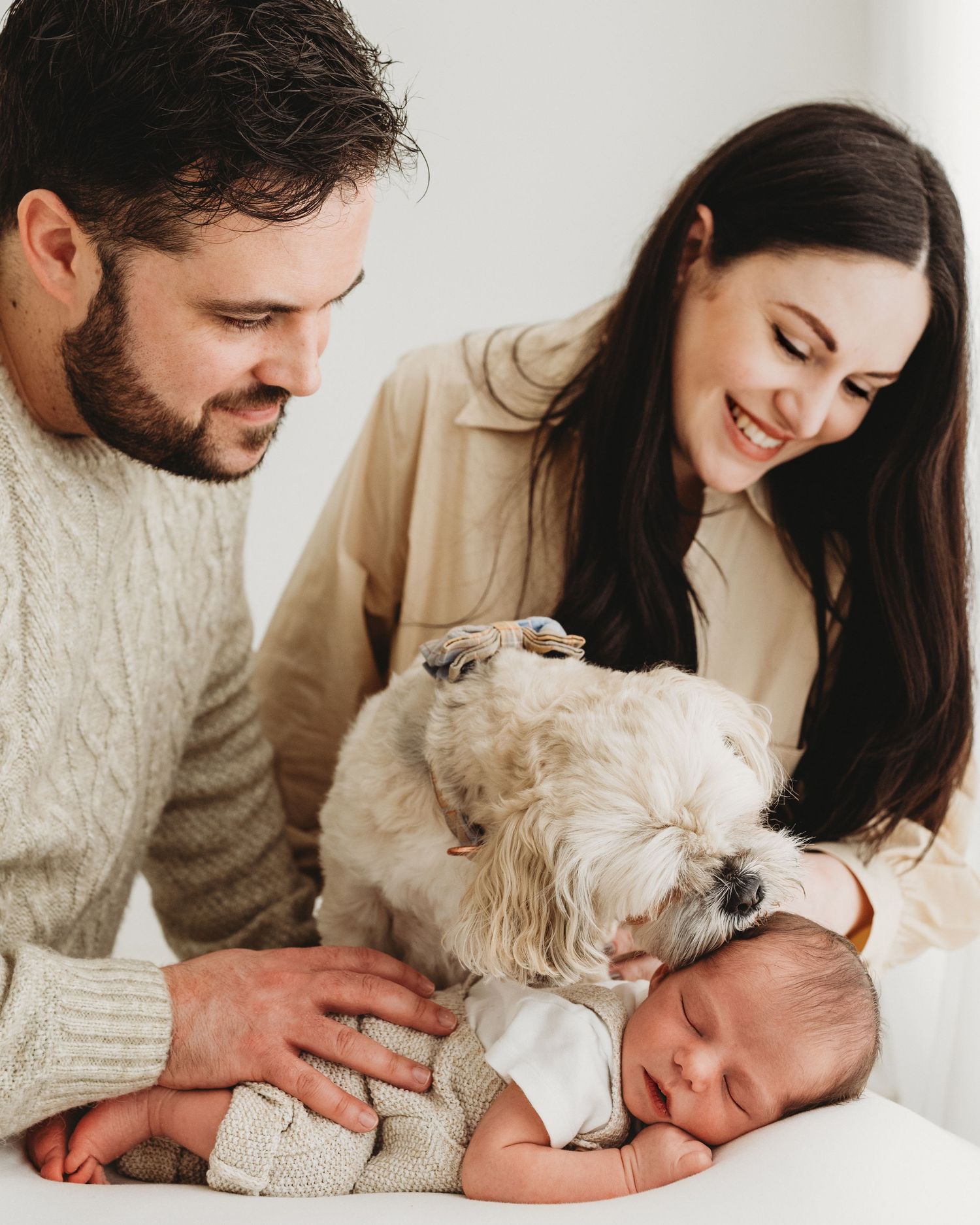 proud parents gaze down at their newborn son as the family dog kisses the top of his head during newborn session in Ayrshire