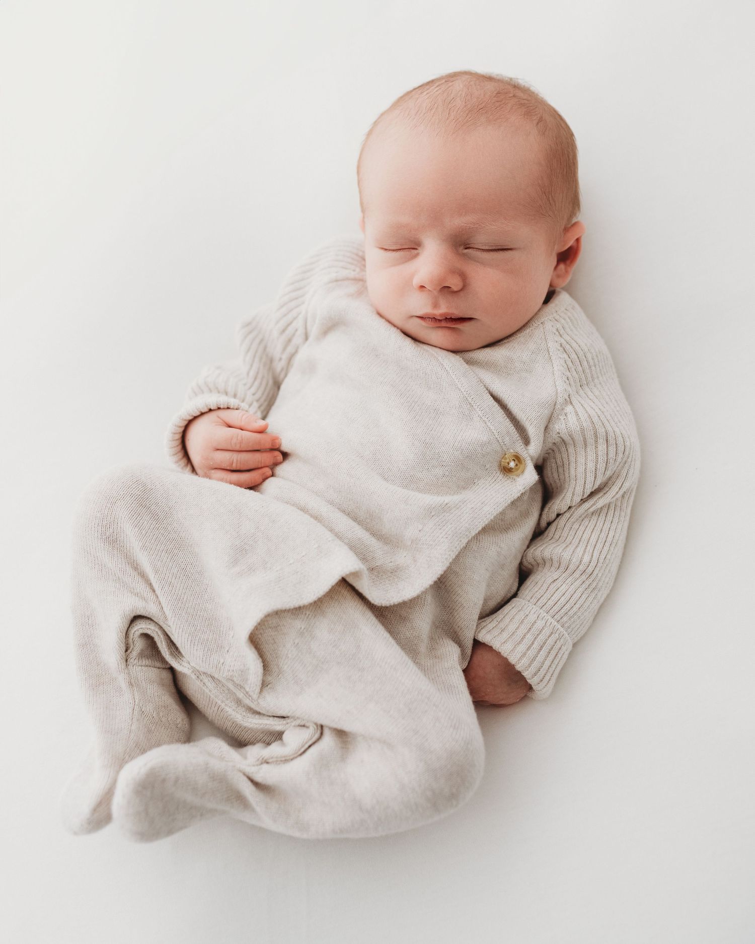 baby sleeps on his back against soft white background, positioned naturally during his Ayrshire newborn photoshoot with Faye McRae