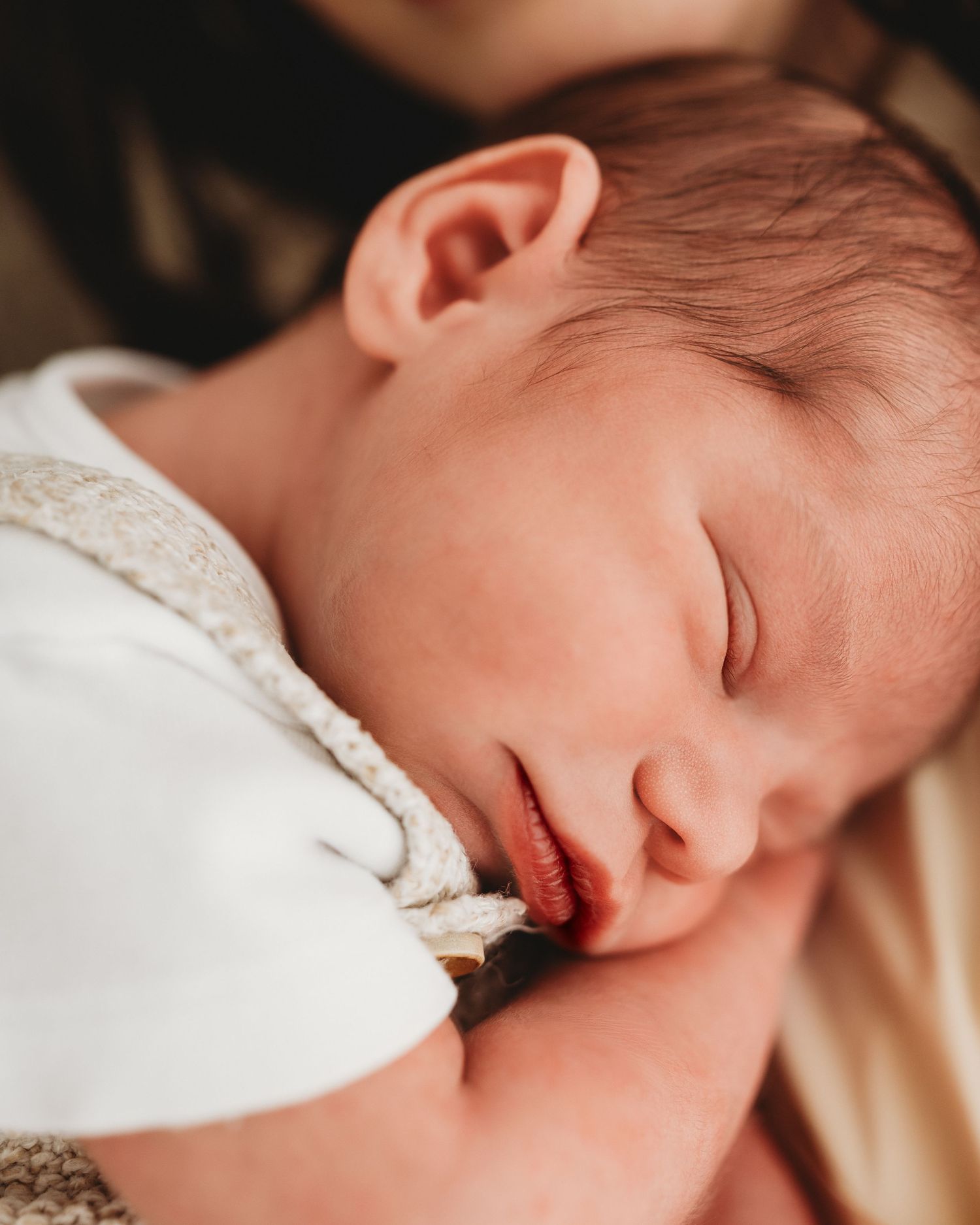 naturally positioned on his mums shoulder, newborn baby smiles softly in his sleep during his natural newborn photoshoot in South Ayrshire