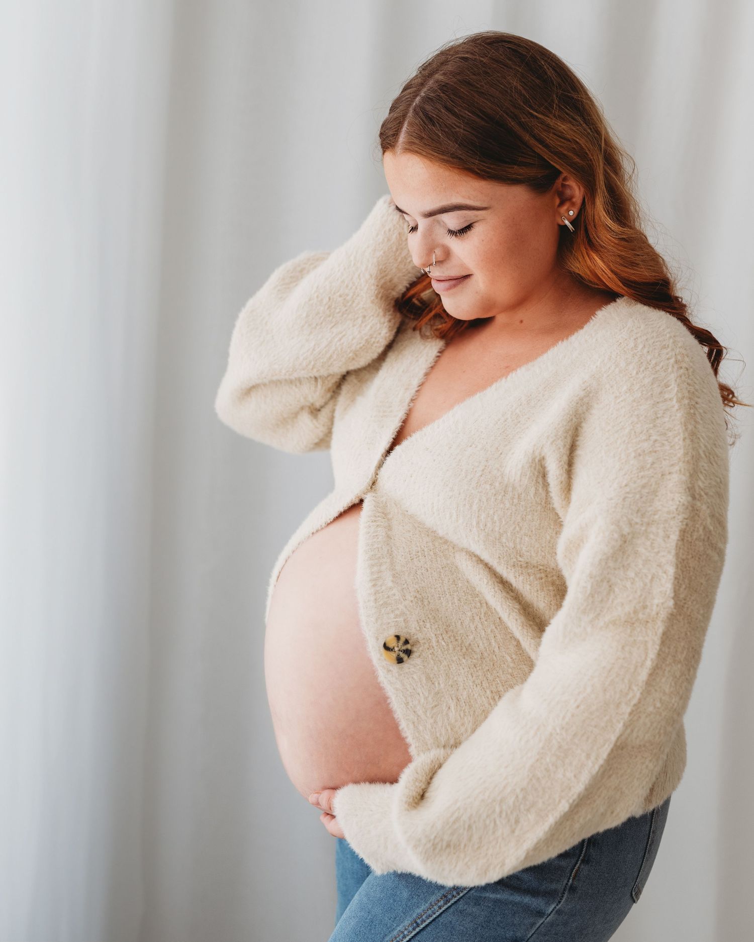 smiling first time mum tucks hair behind her ear as she looks down at her beautiful bump during maternity session in Ayrshire