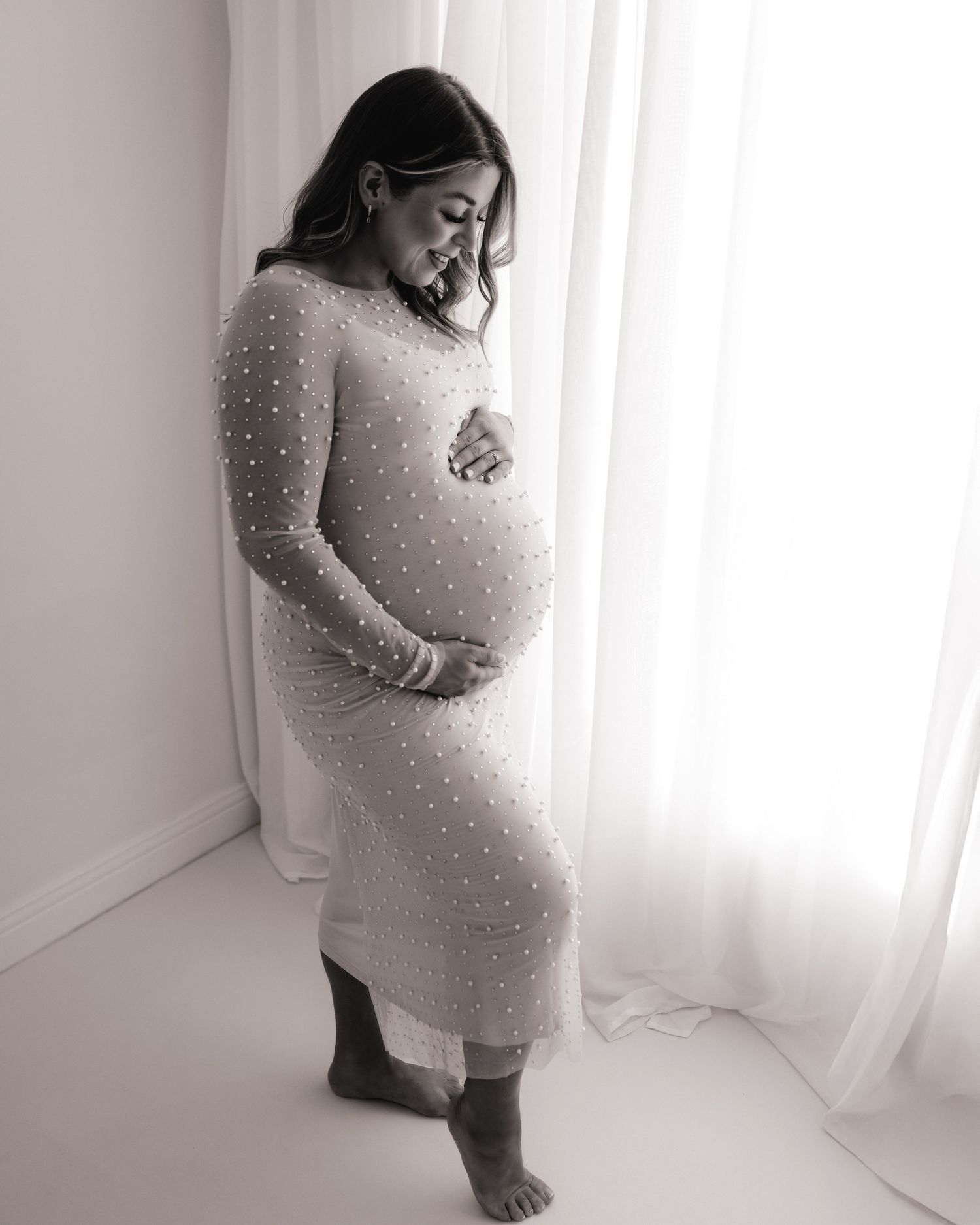 in a form fitting dress, this first time mum cradles her bump looking down during a quiet moment