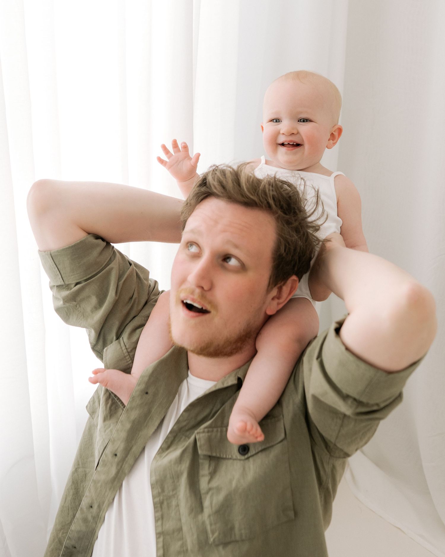 the 1 year old baby laughs sitting on her dads shoulders as they play together during her milestone session celebrating her birthday