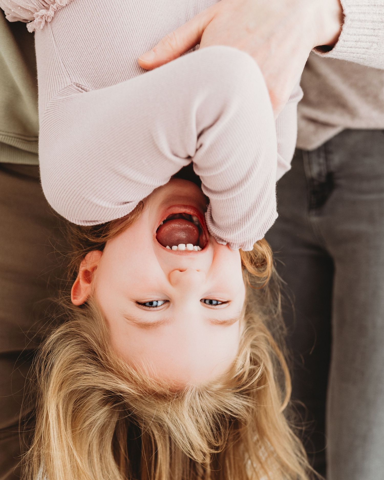 parents hold 4 year old upside down during a play-filled photoshoot in Ayrshire making the young girl laugh naturally