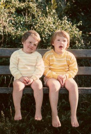 Two sisters sit side by side on a bench looking into the camera as their parents take a photo of a family holiday to remember the moment