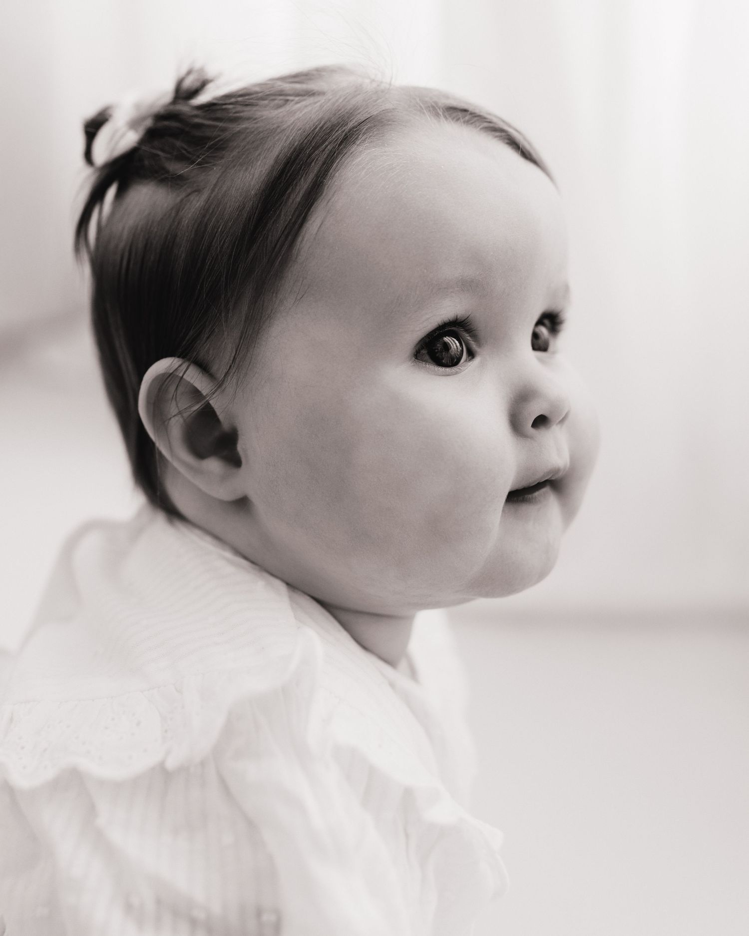 wide eyed 1 year old looks over to her parents, eyes full of love, natural portrait captured by Faye McRae during a milestone session in Ayr