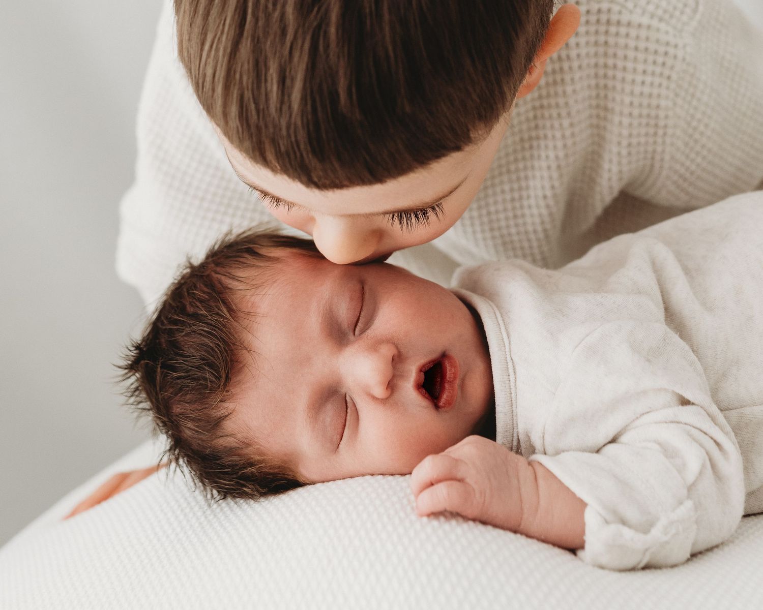 big brother leans down to kiss his sleeping new baby sister during natural newborn photoshoot in South Ayrshire with Faye McRae