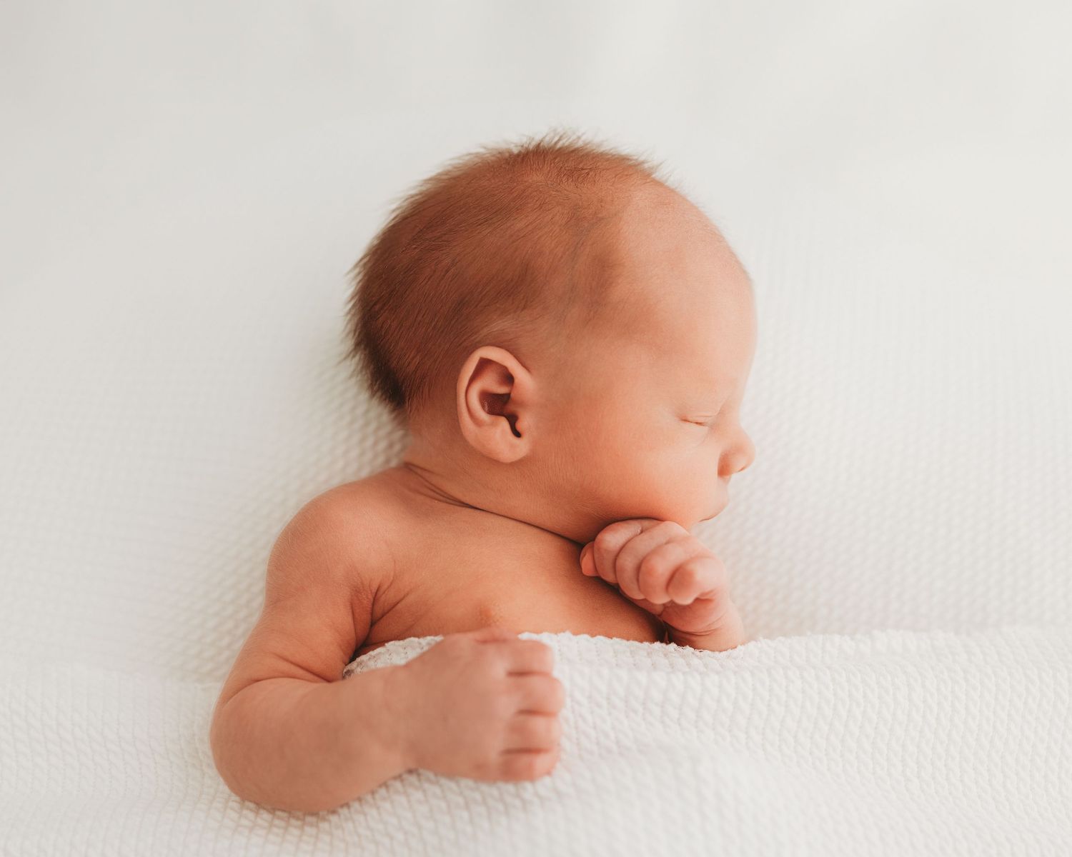 Newborn baby sleeps soundly on his back in Ayrshire, positioned naturally under a blanket the focus of the image is entirely on the baby