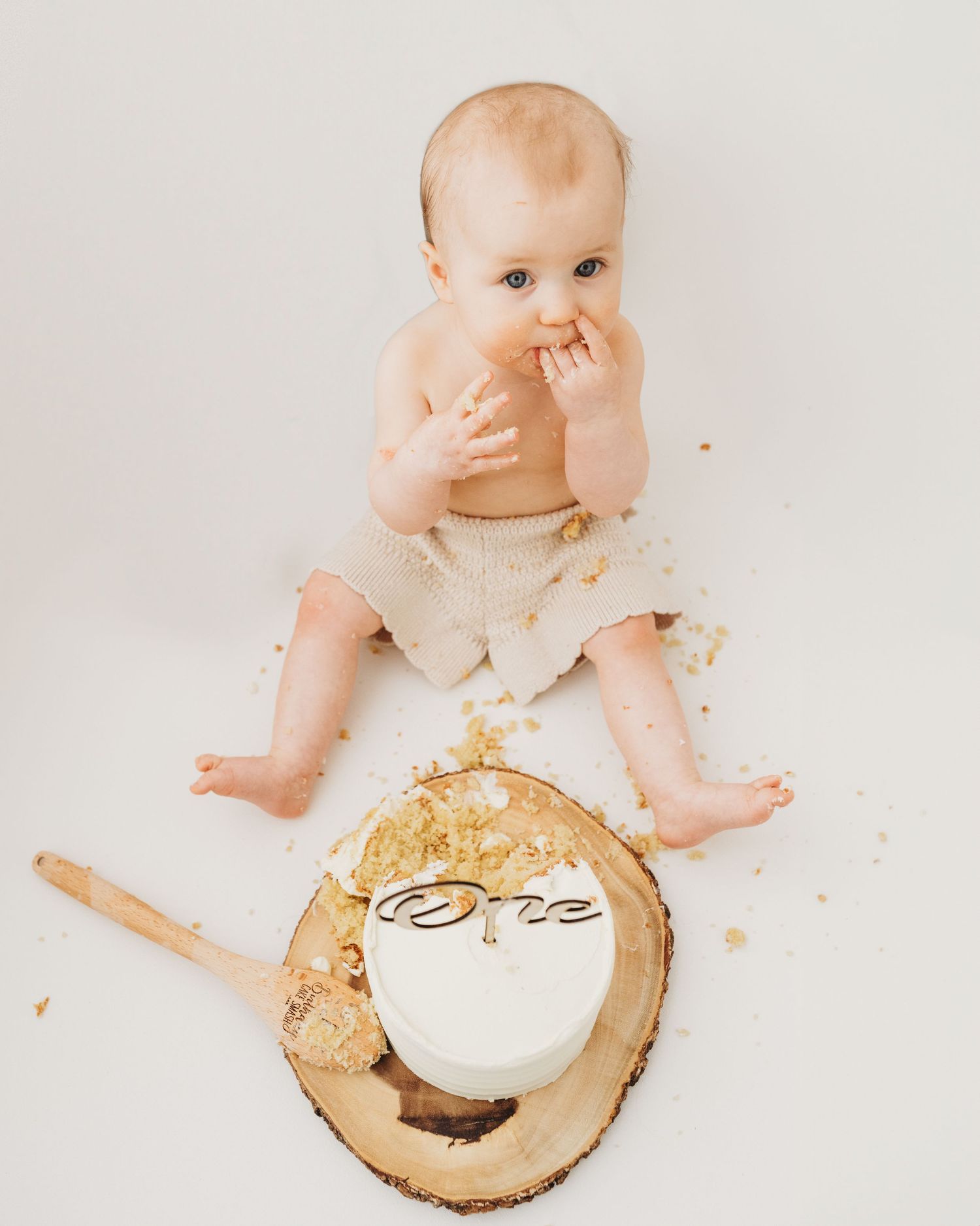 baby sits by cake looking up at camera during 1st birthday photoshoot in South Ayrshire