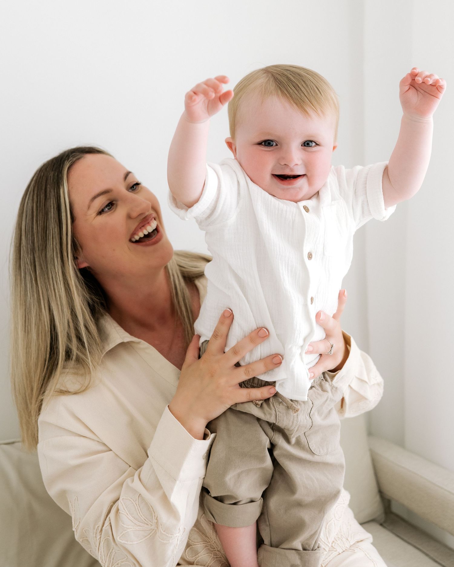 1 year old baby boy has his arms in the air in excitement as his beautiful mum smiles on full of joy and so much love for her little boy