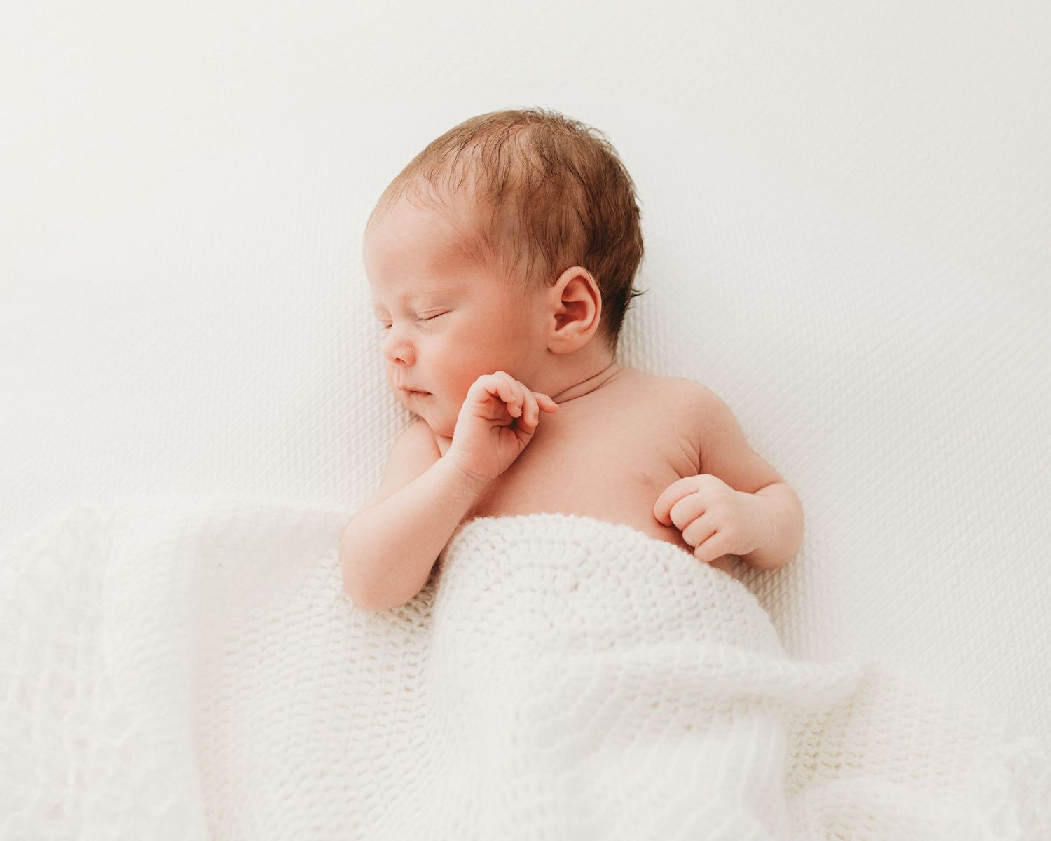 peaceful newborn baby girl lays on her back under a handmade blanket