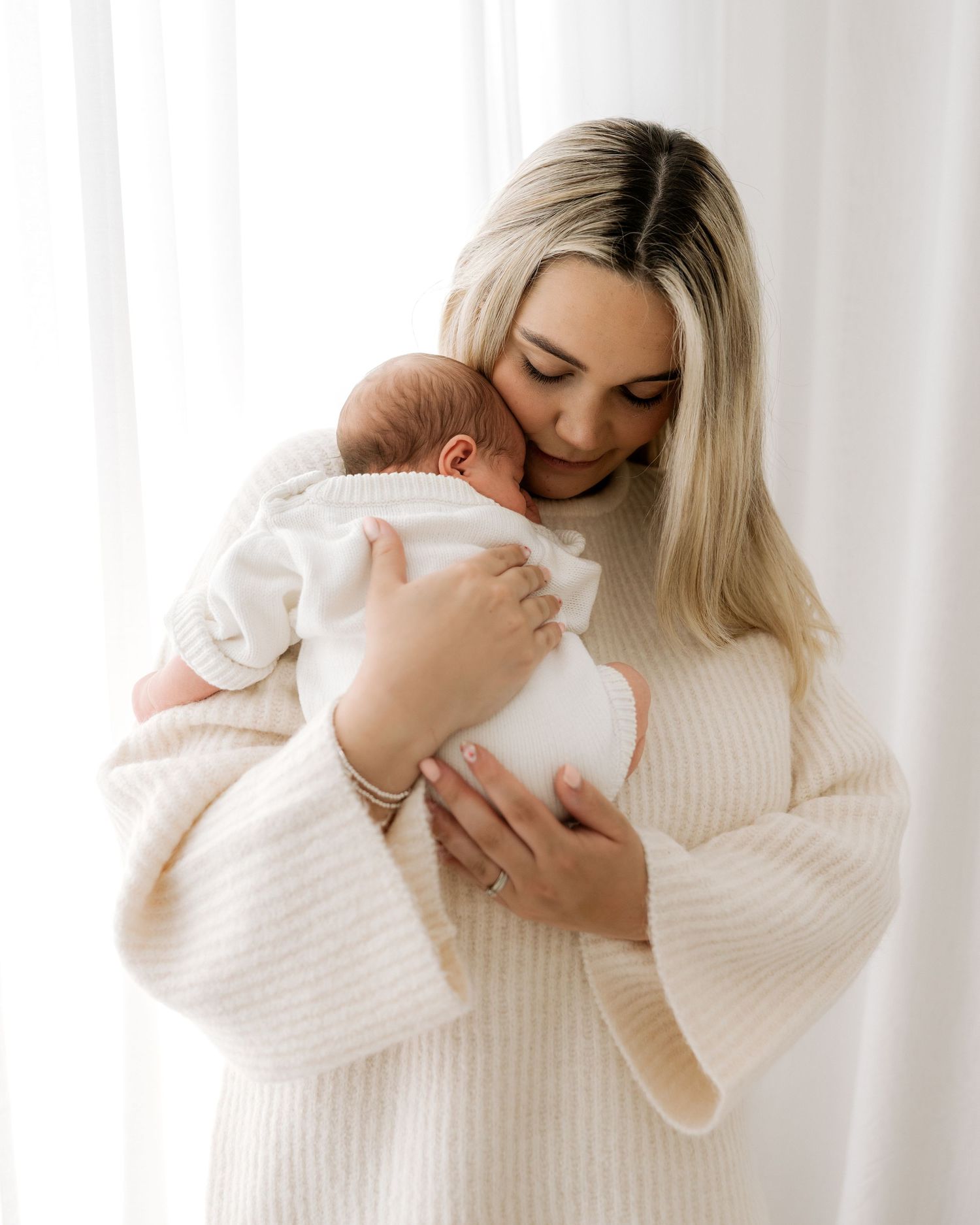 first time mum cradles her newborn baby girl against her chest, her baby scrunched up and nestled into her neck, a quiet tender moment