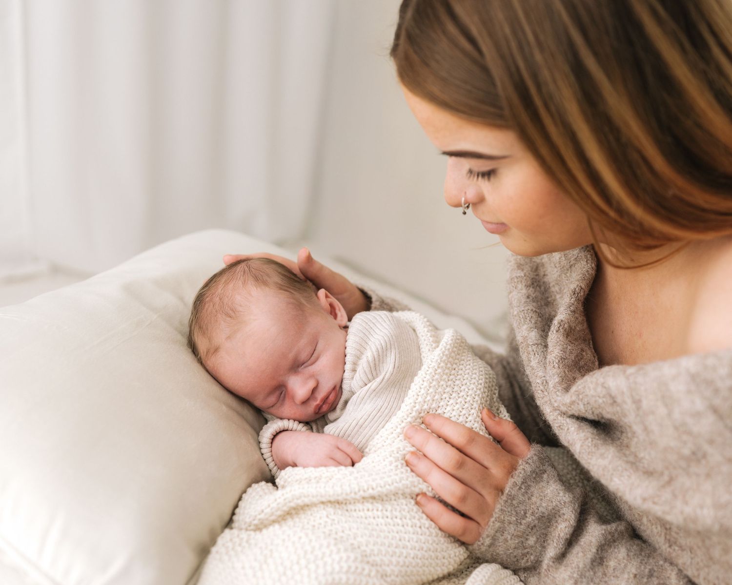 newborn baby sleeps peacefully curled up against a cushion, watched proudly by his mum who is full of love in Ayrshire photography studio