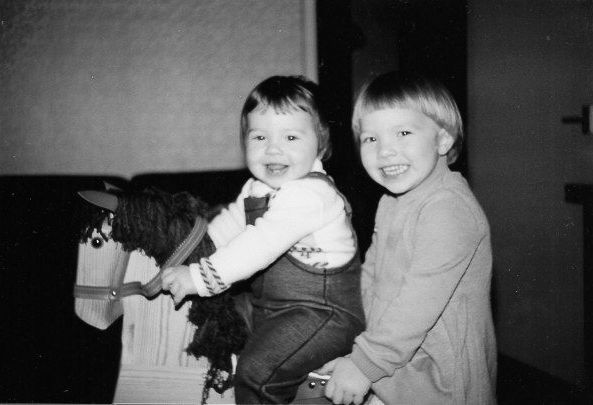 Two sisters sit on a wooden rocking horse smiling into the camera as a family memory is captured