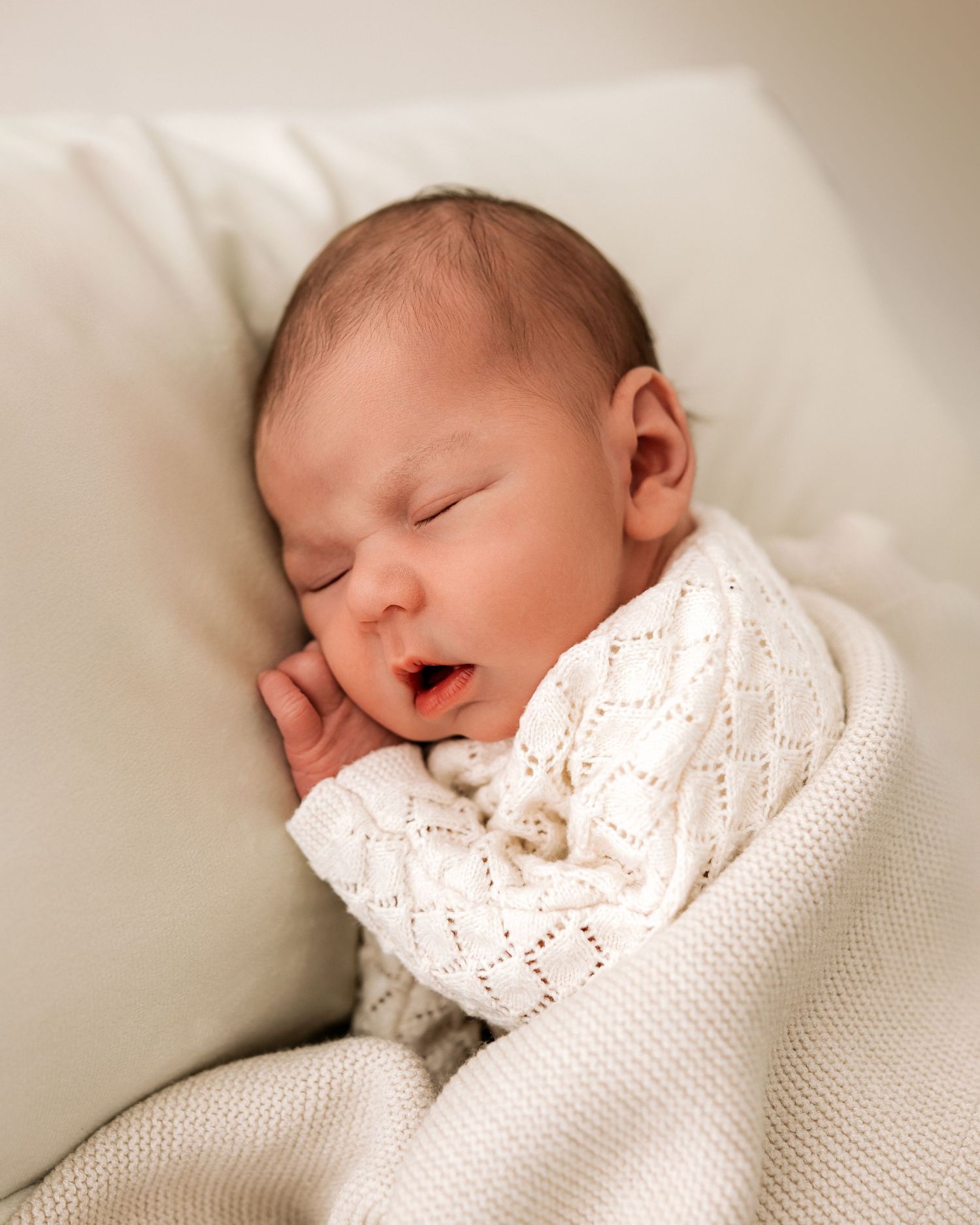 beautiful newborn baby girl sleeps against pillow, under a knitted blanket during her natural newborn photoshoot in Ayrshire