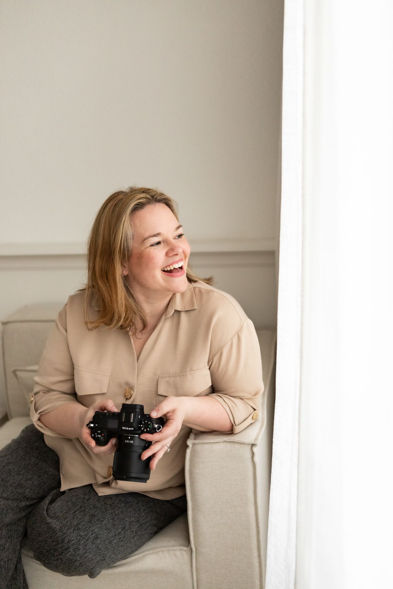 Faye McRae photographer looks laughing and smiling out her Ayrshire studio window holding her camera