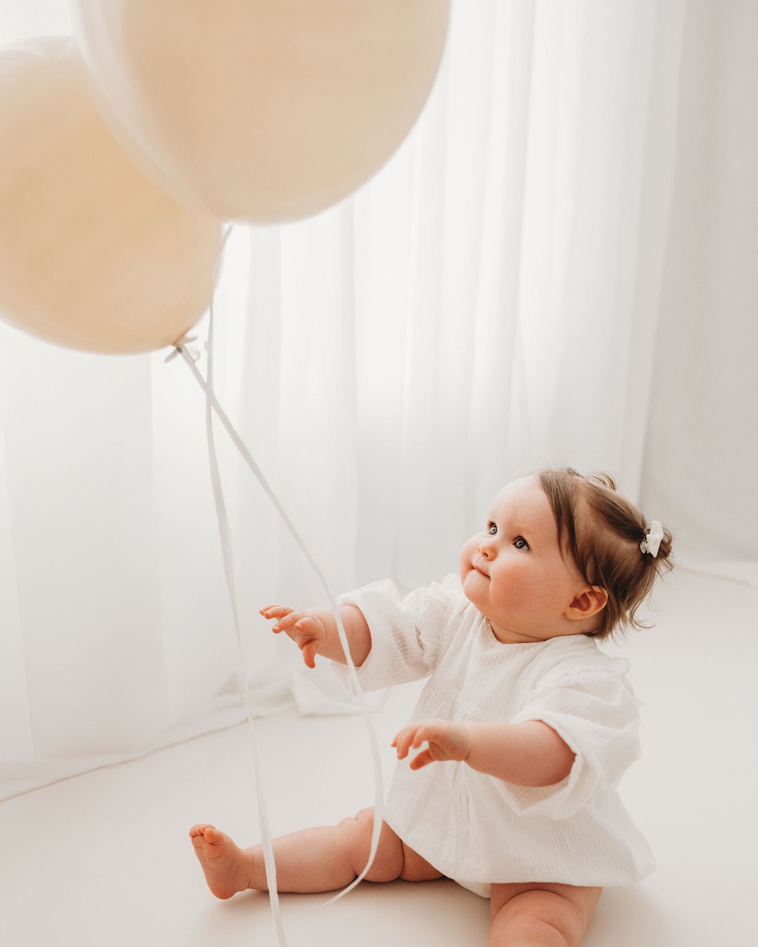 reaching for 2 balloons, baby girls eyes are full of wonder and curiosity during her 1st birthday photoshoot in Ayrshire