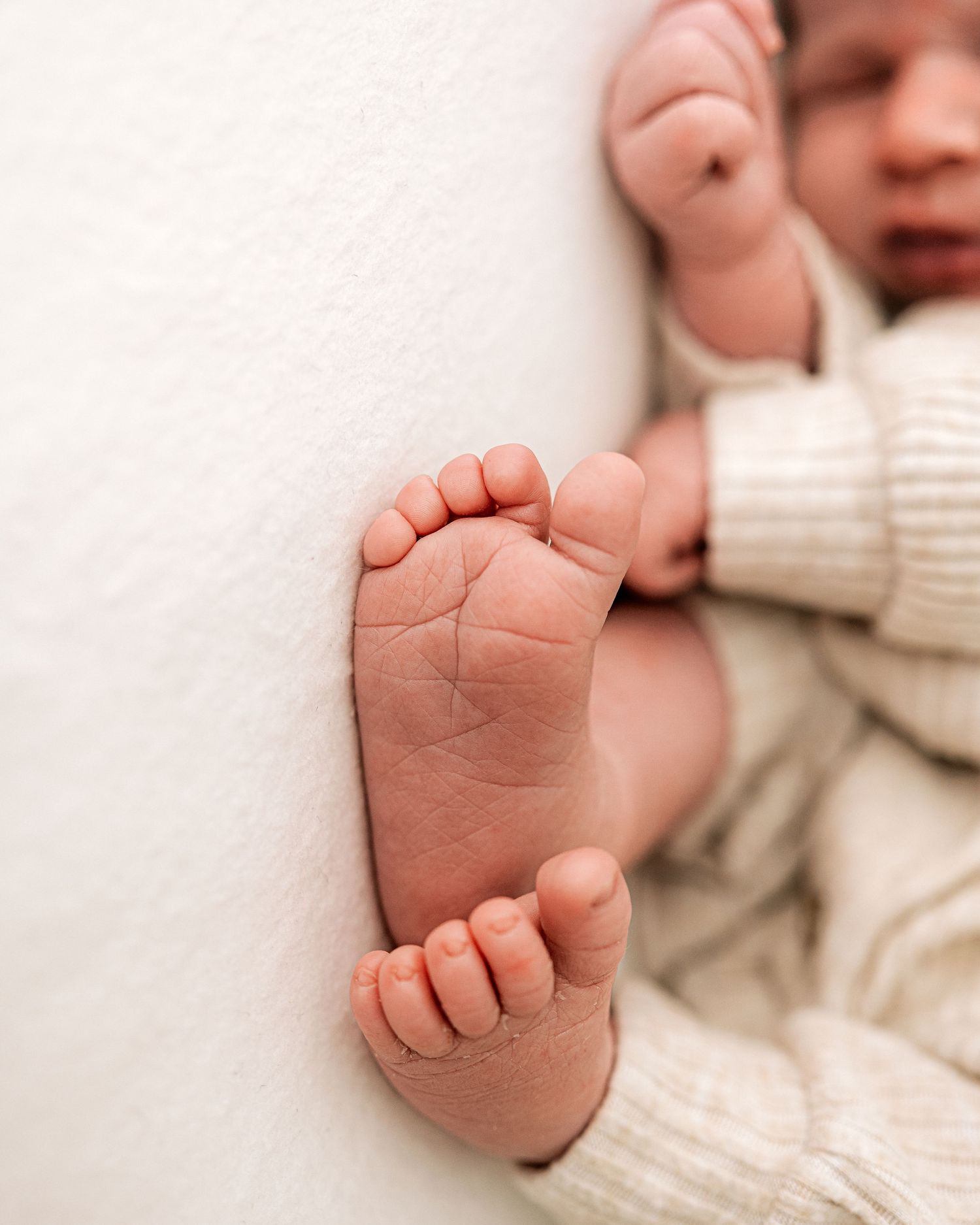 newborn baby sleeps soundly as focus is on her tiny feet during her natural newborn session in Faye McRae's all-white Ayrshire studio