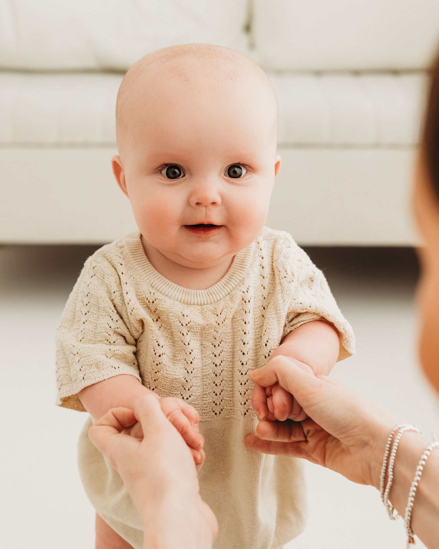 holding mums hands for reassurance, 6 month old smiles happily during milestone session in South Ayrshire photography studio