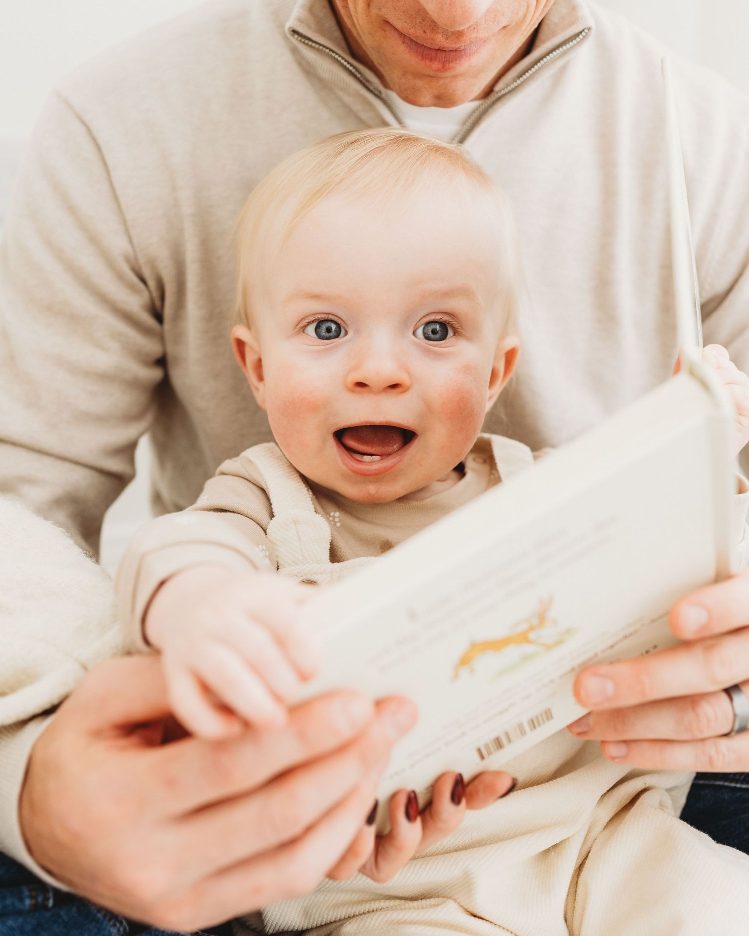 excited and animated 1 year old reads a book with his dad during a family photoshoot in Ayrshire