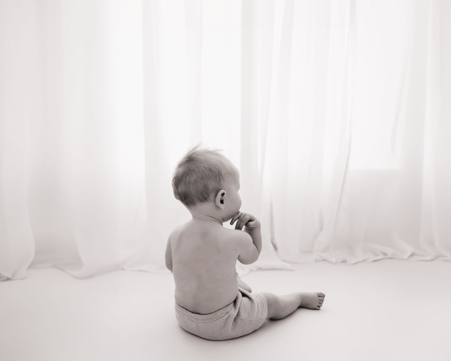 with his back to the camera, 9 month old baby has fingers in his mouth, sitting calmly during a quiet moment in Ayrshire milestone session