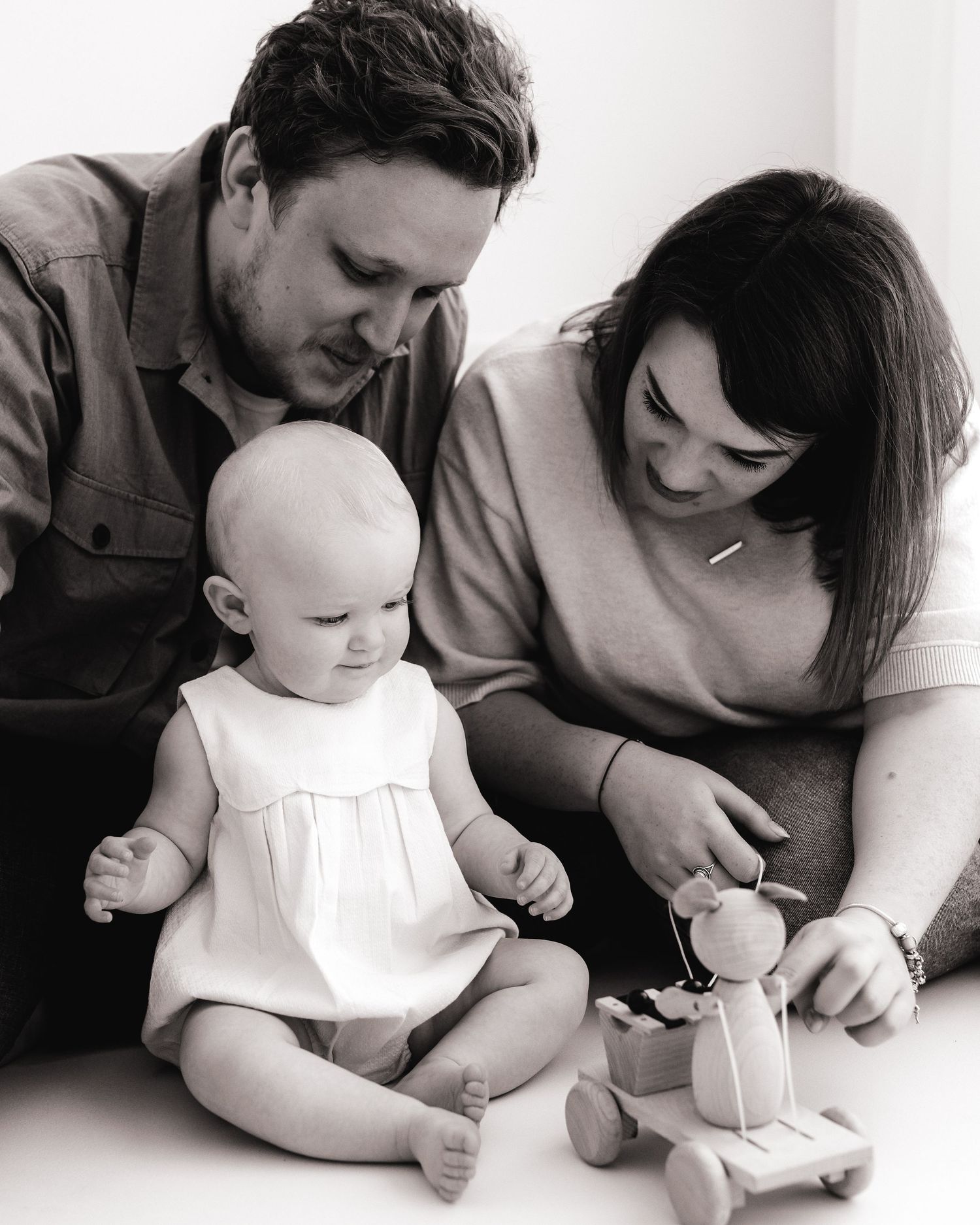 black and white family portrait of some quiet playtime, exploring the world together, playing with wooden toys on the all-white studio floor