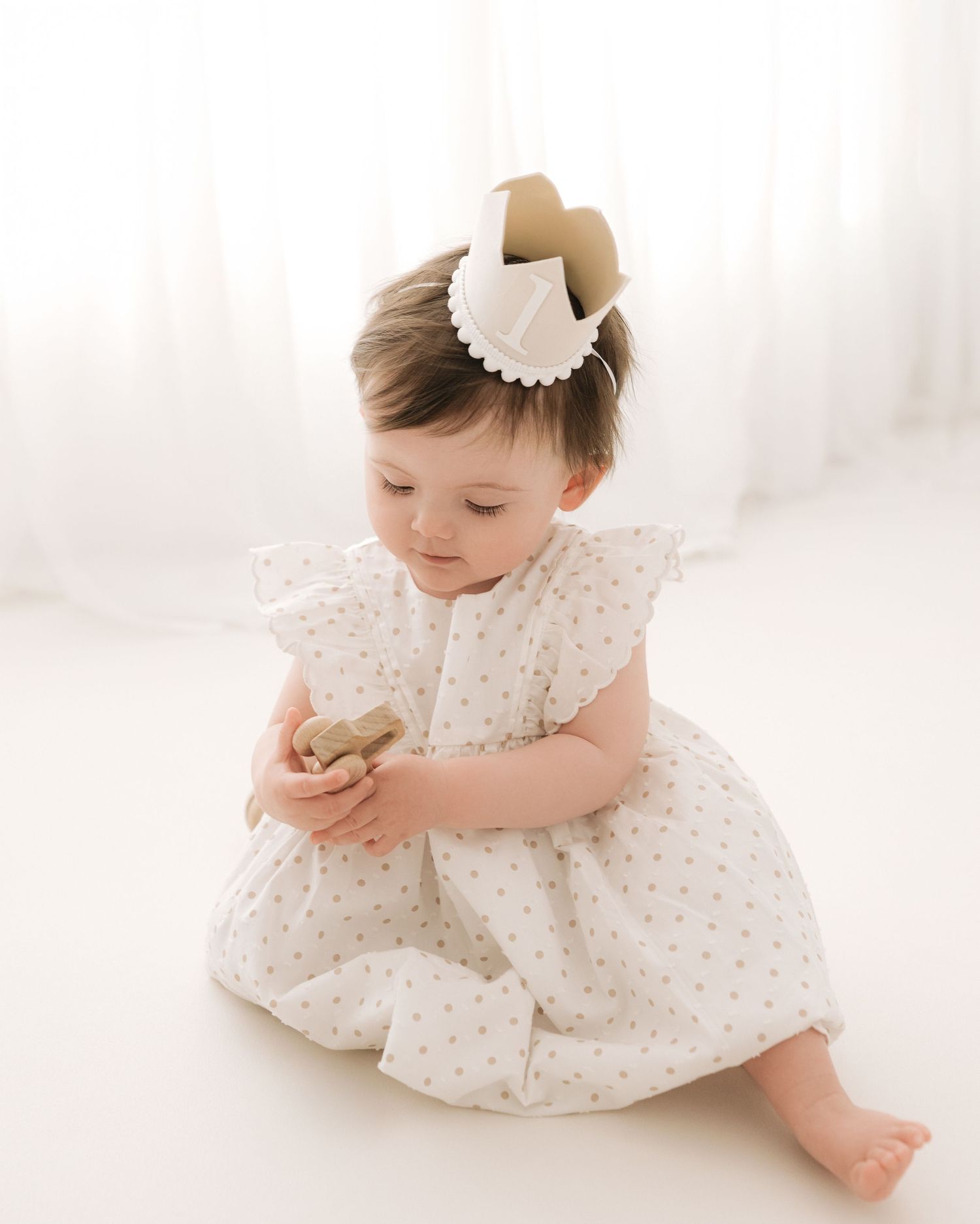 looking down and playing with a wooden toy, baby girl celebrates turning 1 in South Ayrshire's timeless, authentic photography studio