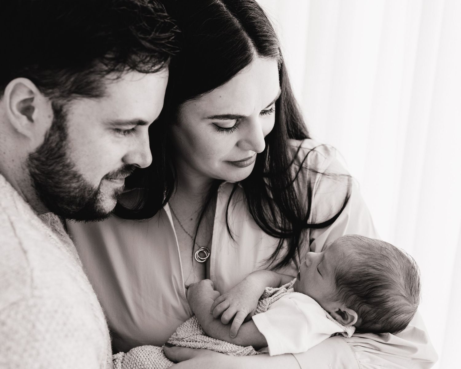 first time parents gaze lovingly down at their new baby in this timeless black and white portrait captured in Ayrshire's all-white studio