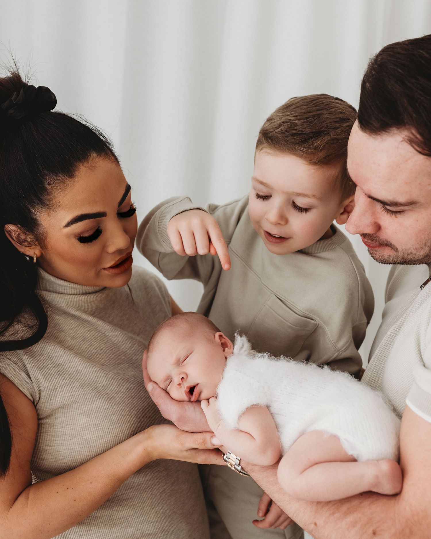mum dad and big brother gaze down at new baby girl who sleeps soundly on dads arm during newborn session in Ayrshire photography studio