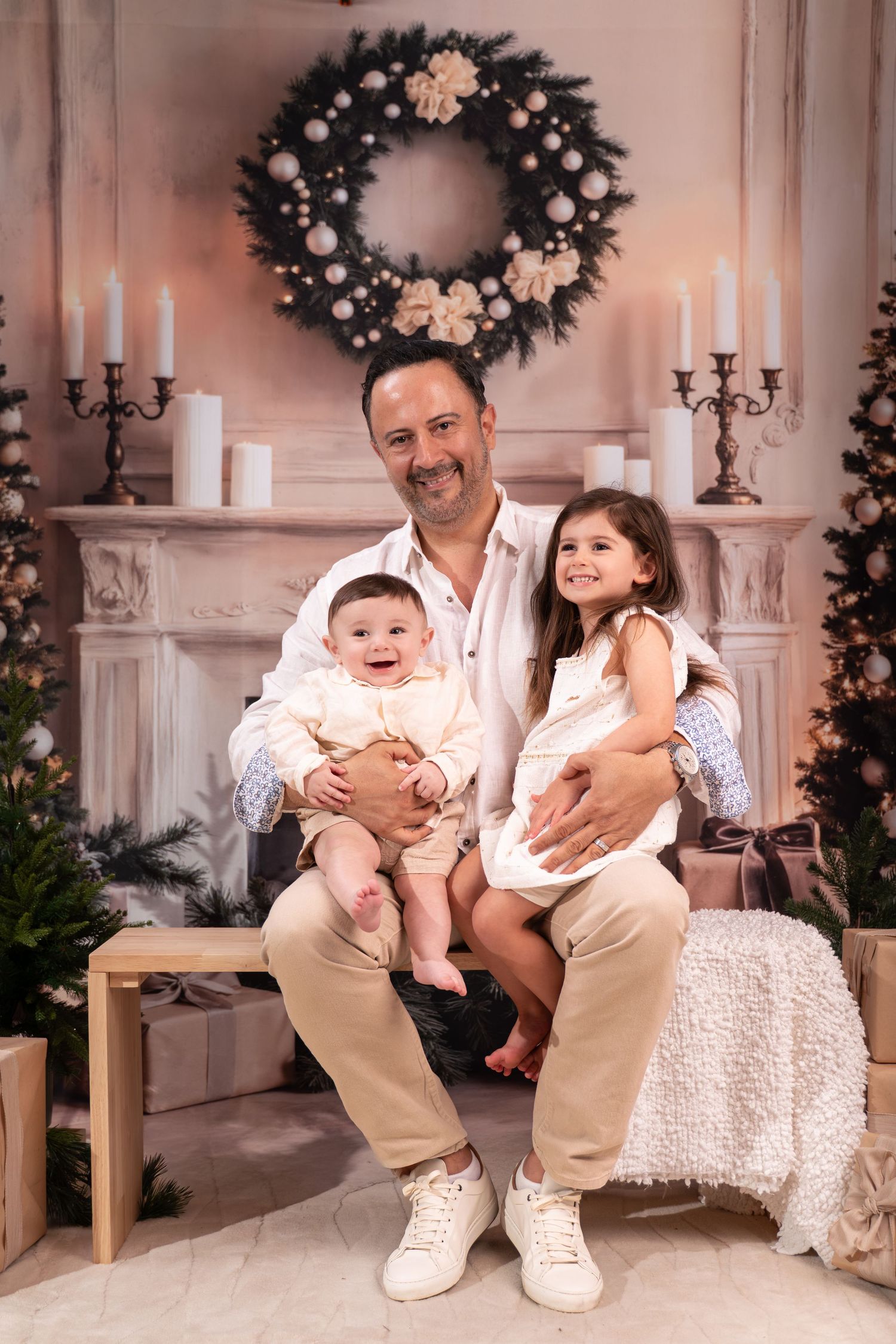 A family poses together in a cozy holiday setting with white Christmas decorations and wreaths in the background.
