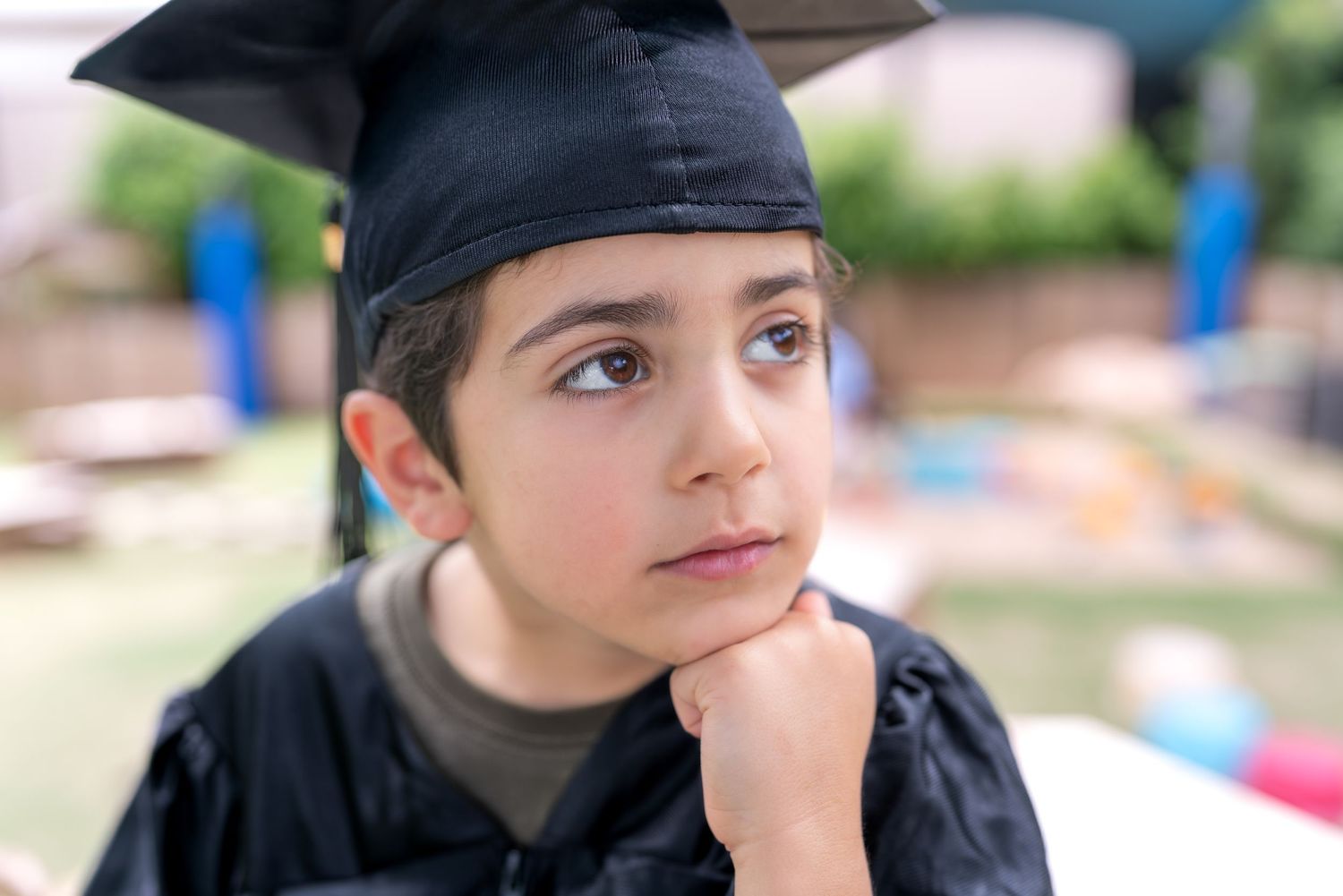 A person in a black hoodie gazes thoughtfully into the distance while resting their chin on their hand.