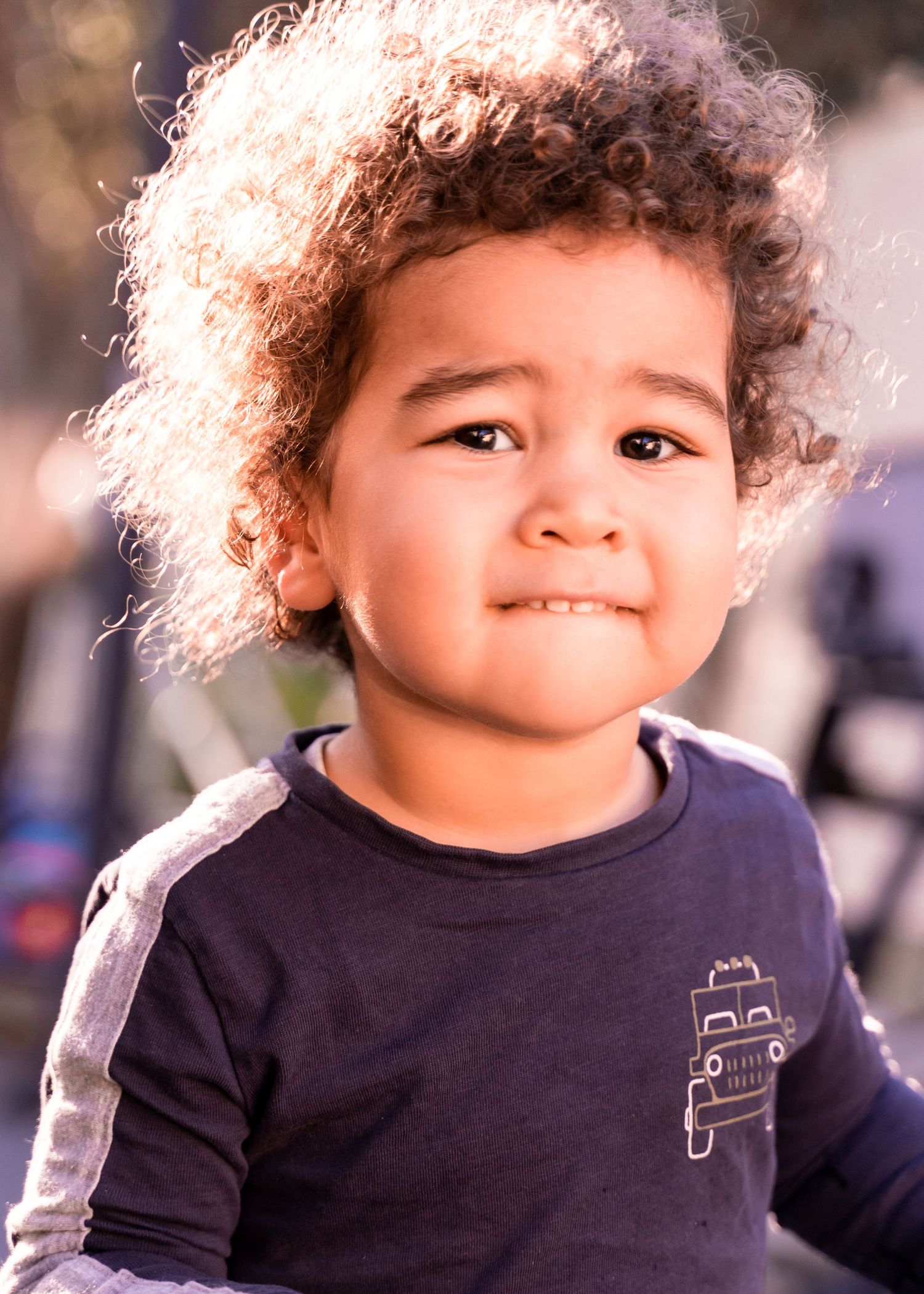 A child in a navy shirt with curly hair smiles in warm lighting.