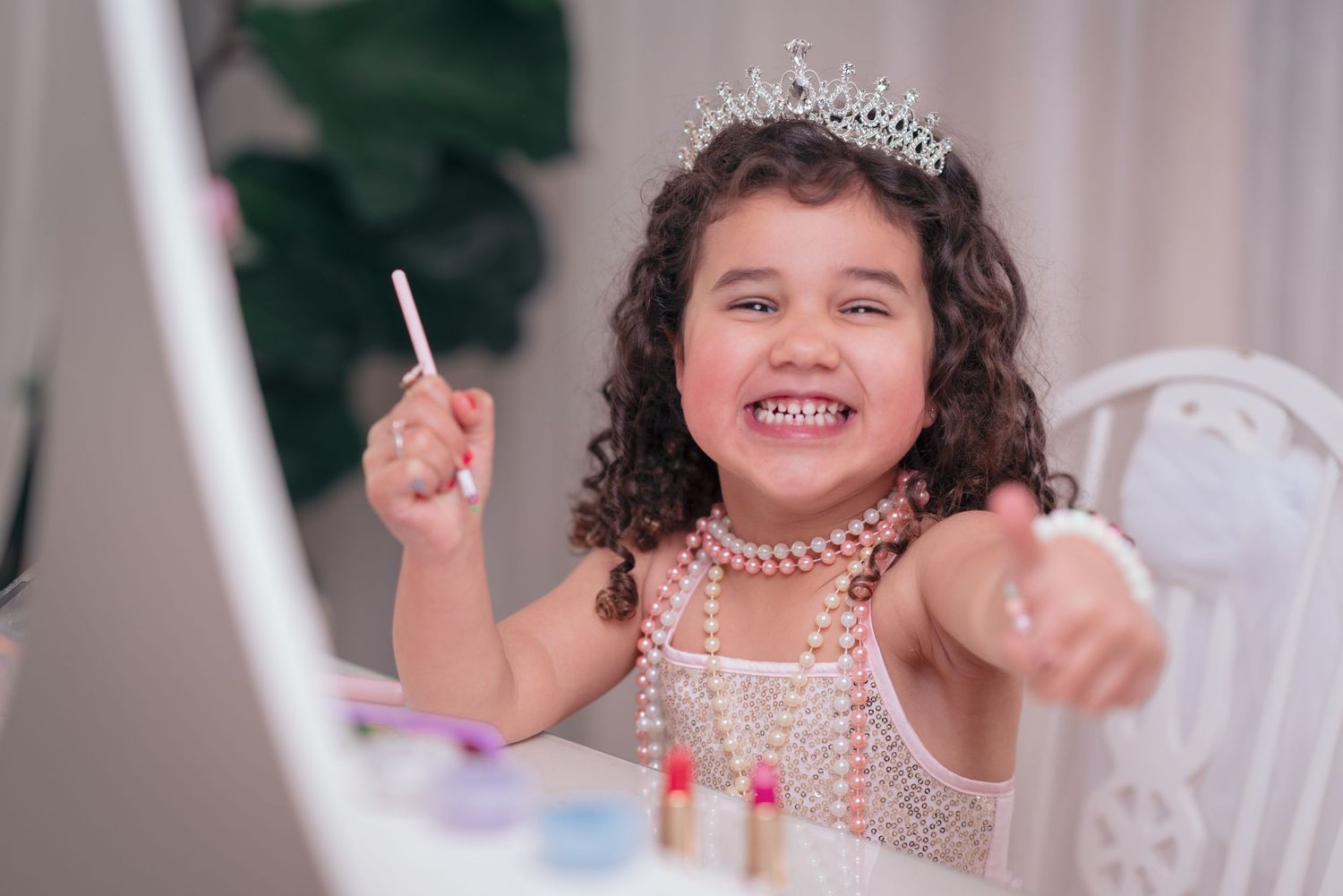 A child in a white dress and pearl necklace smiles while sitting at a table with decorative decor.