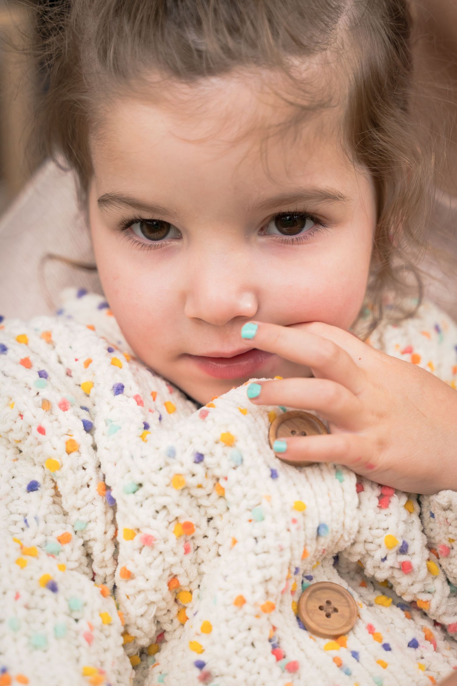 A child in a floral print sweater touches their face while looking at the camera.