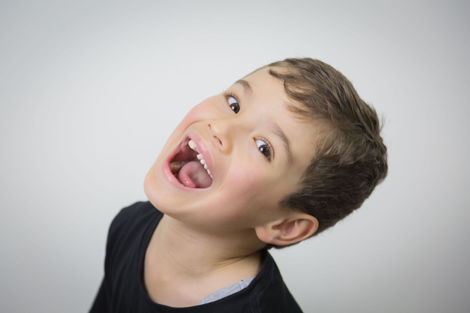 A child makes a silly expression while looking up against a gray background.