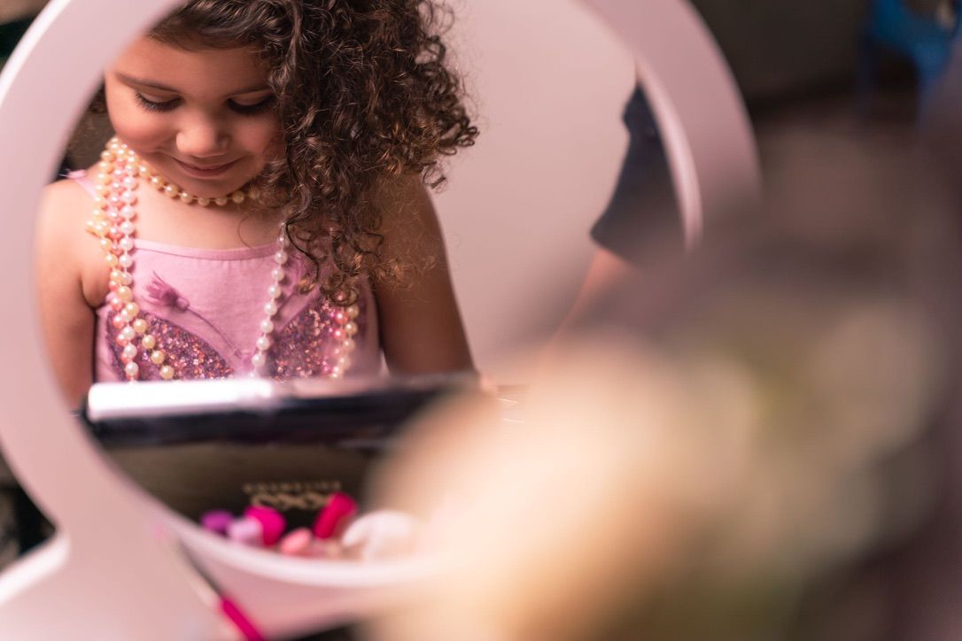 A reflection in a decorative mirror shows someone wearing pearls and a pink dress.